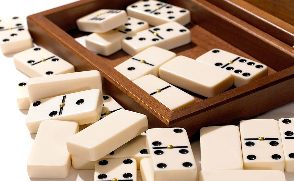 Domino 桌布 壁紙 — 奶油色的多米諾骨牌帶有黑色圓點，從拋光木盒中灑落在明亮的白色背景上。