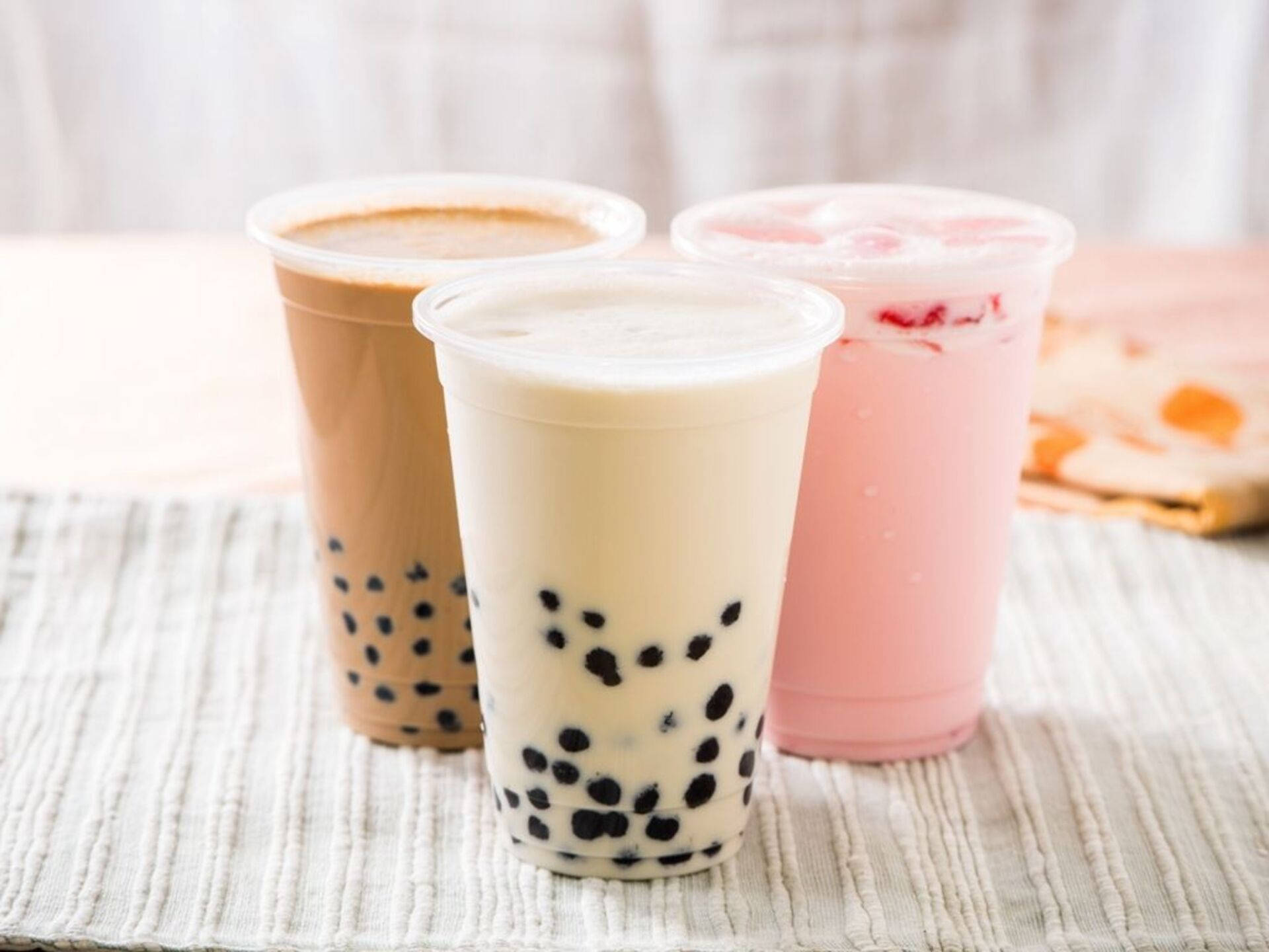 奶茶最愛三重奏 壁紙 — 三杯色彩繽紛的珍珠奶茶放在有紋理的白色墊子上，背景柔和模糊。