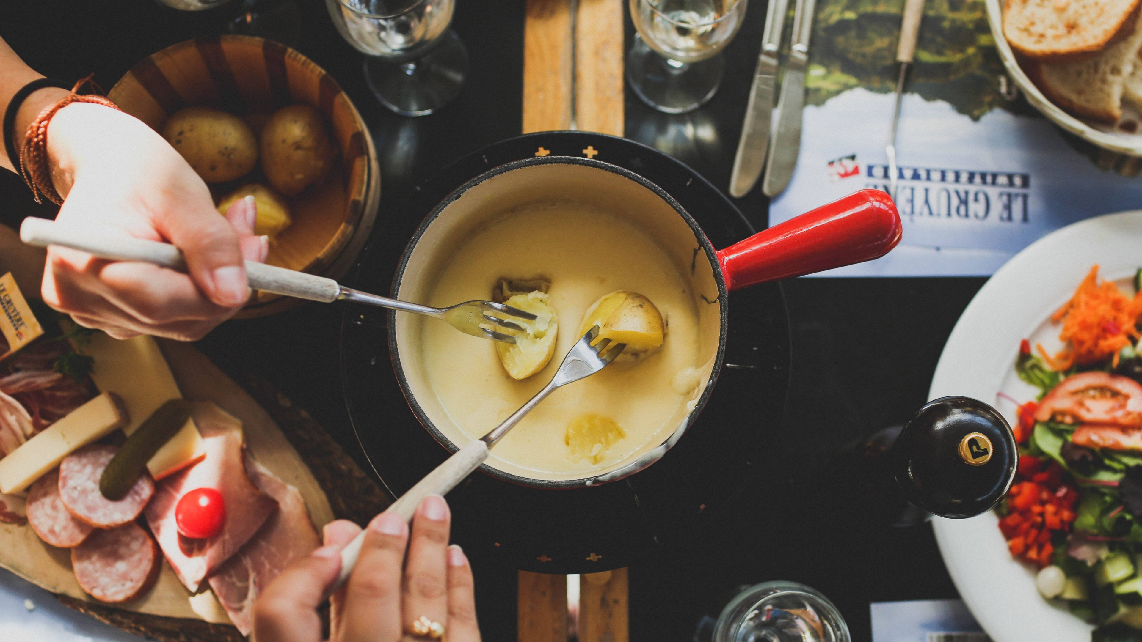 奶酪濃湯與大理石馬鈴薯 壁紙 — Overhead view of hands dipping boiled potatoes into a bubbling cheese fondue pot surrounded by meats bread and salad.