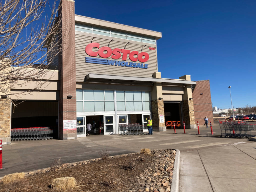 Costco Wholesale商店入口，購物者和購物車在晴朗的藍天下。