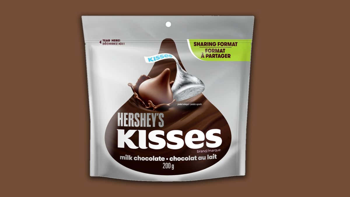 好時之吻巧克力品牌圖像 壁紙 — 一個銀色袋裝的 Hershey's Kisses 牛奶朱古力糖果，帶有融化吻圖案，背景為棕色。