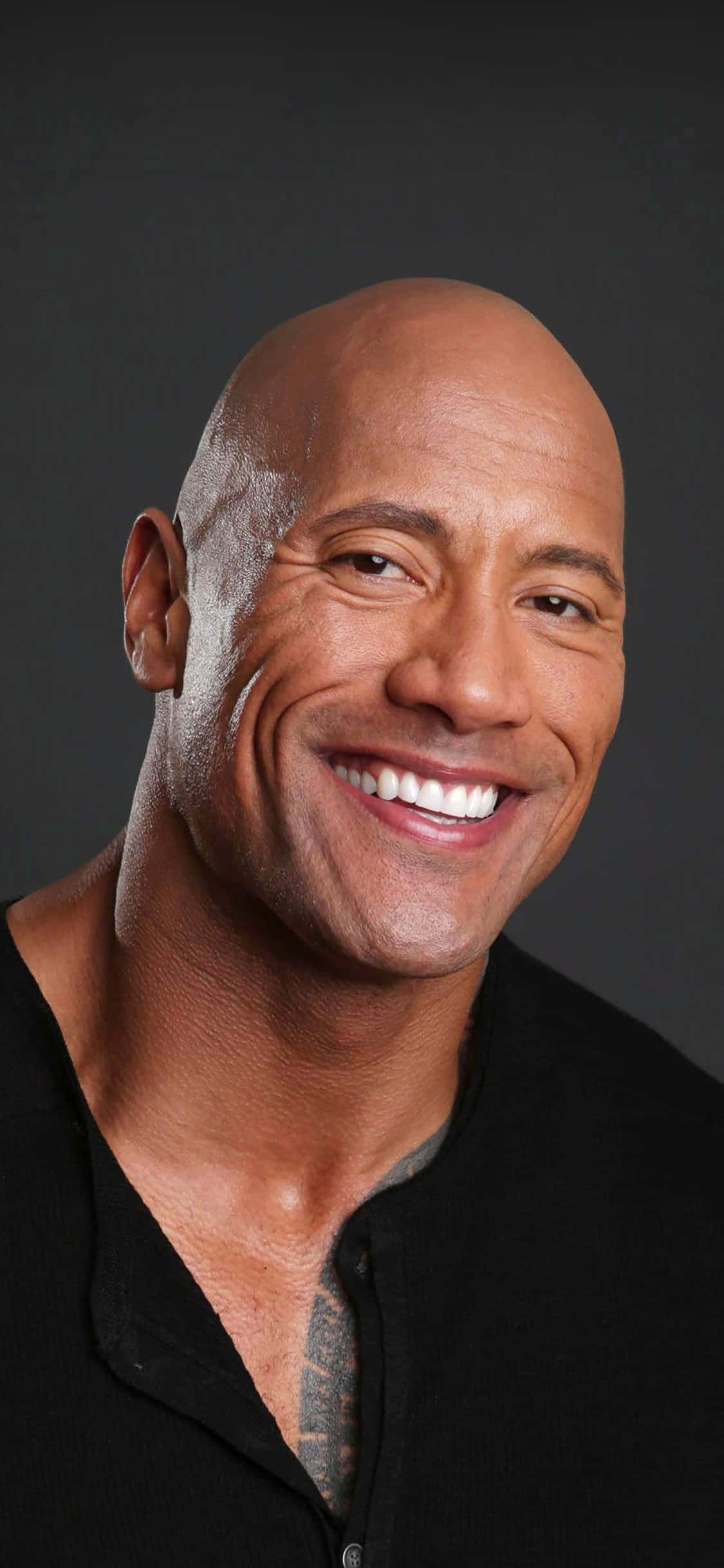 好萊塢 A 級明星享受奢華生活 壁紙 — Dwayne Johnson 嘅特寫肖像，喺深灰色嘅工作室背景前燦爛微笑。