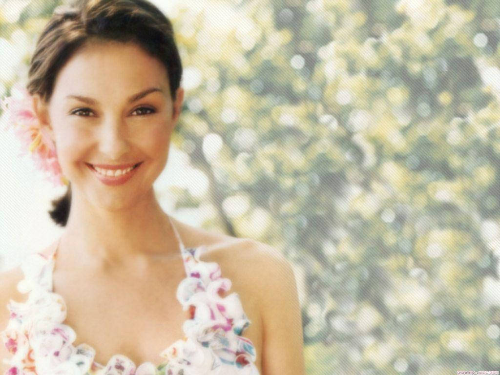 一位頭髮上插著粉紅花的女子，在戶外穿著花卉圖案上衣微笑。