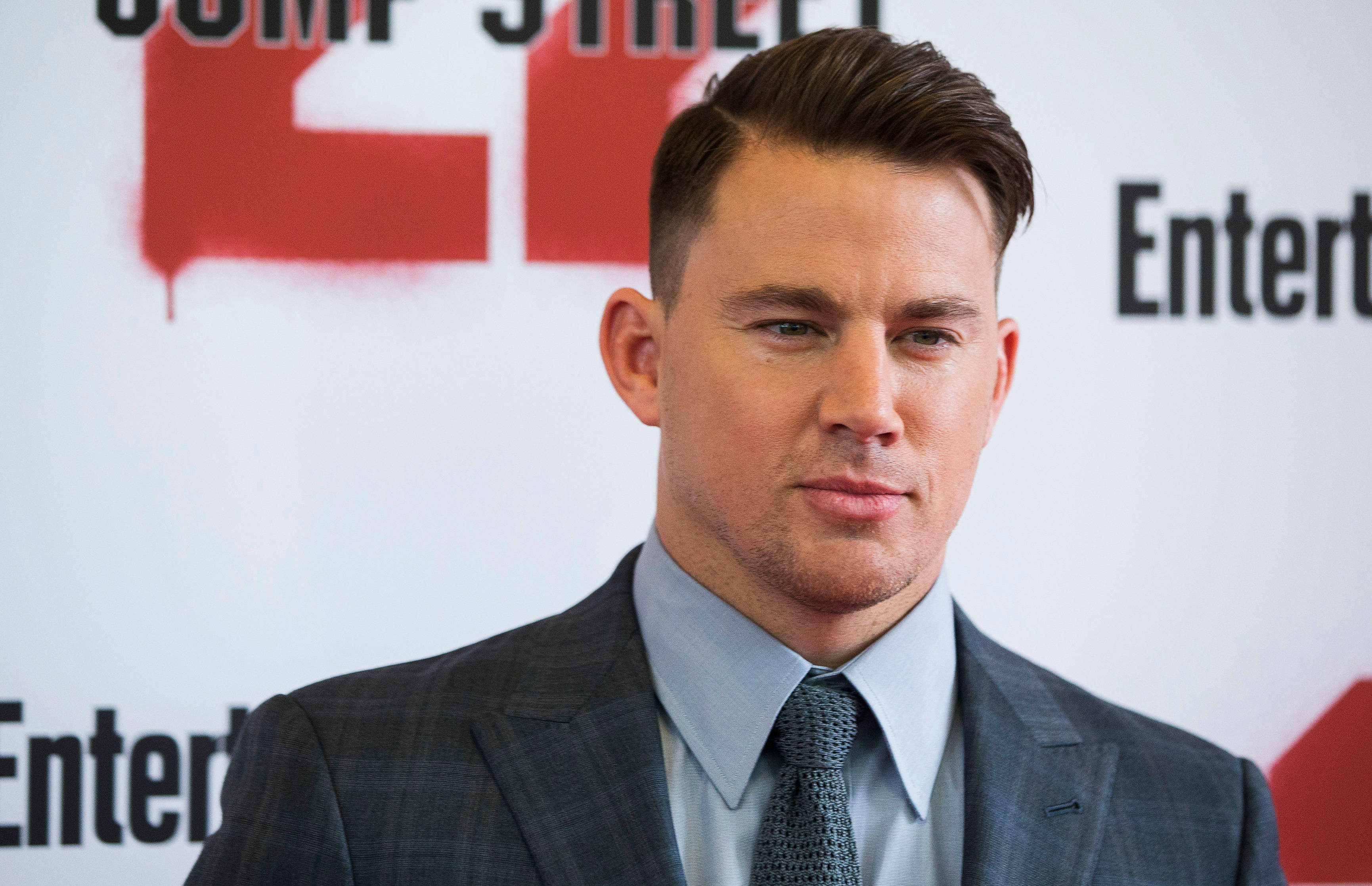 好萊塢巨星錢納·塔圖姆 壁紙 — Channing Tatum 身穿俐落灰色西裝打領帶，在背後有 'Entertainment Weekly' 品牌的紅地毯活動上自信擺姿勢。