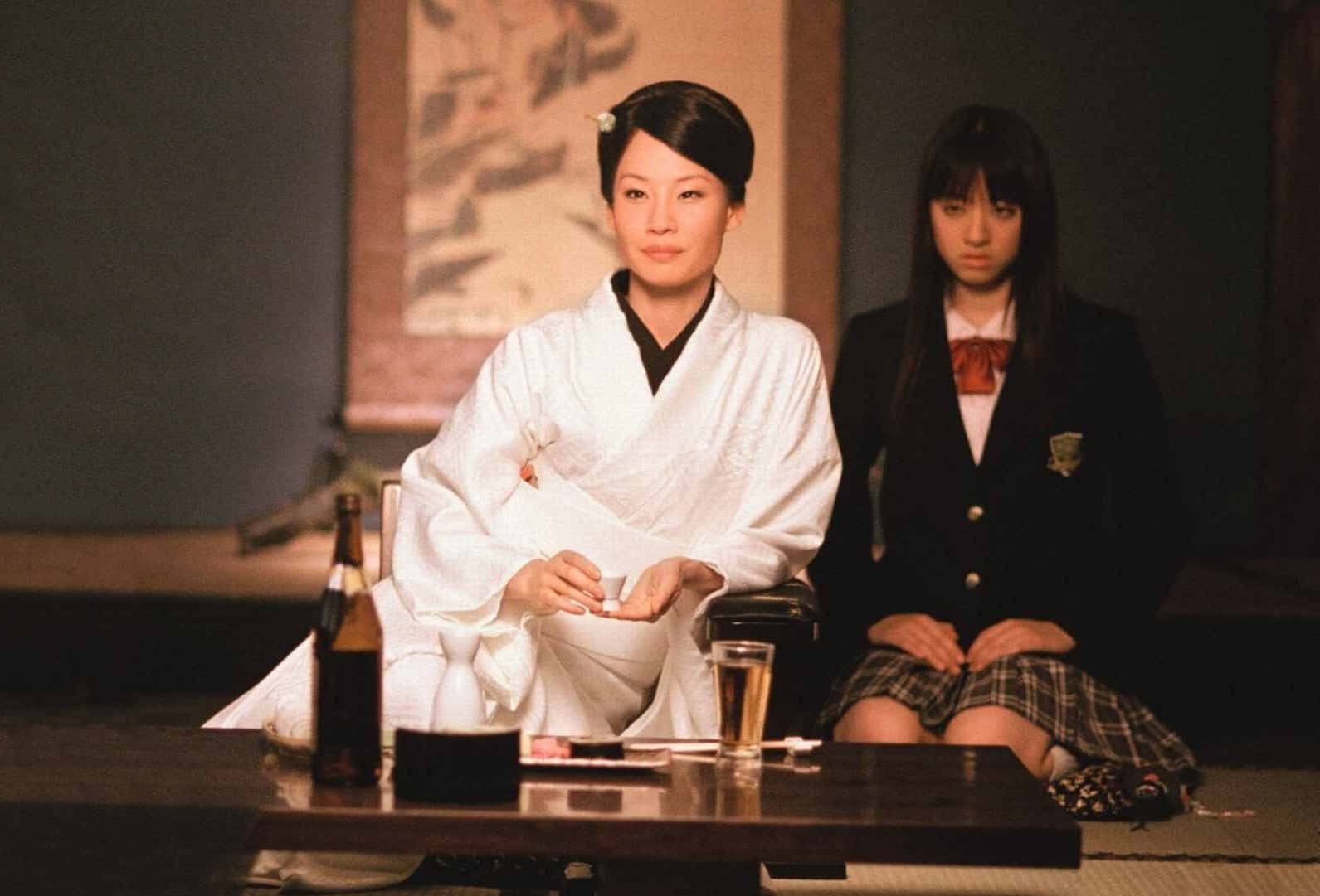 兩位穿著傳統服裝和校服的女性在室內矮桌旁就座。