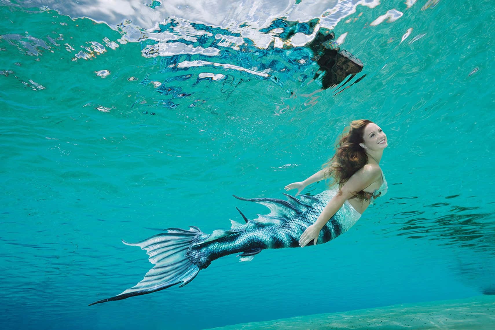 一位擁有美人魚尾巴的女性在碧綠水中游泳。