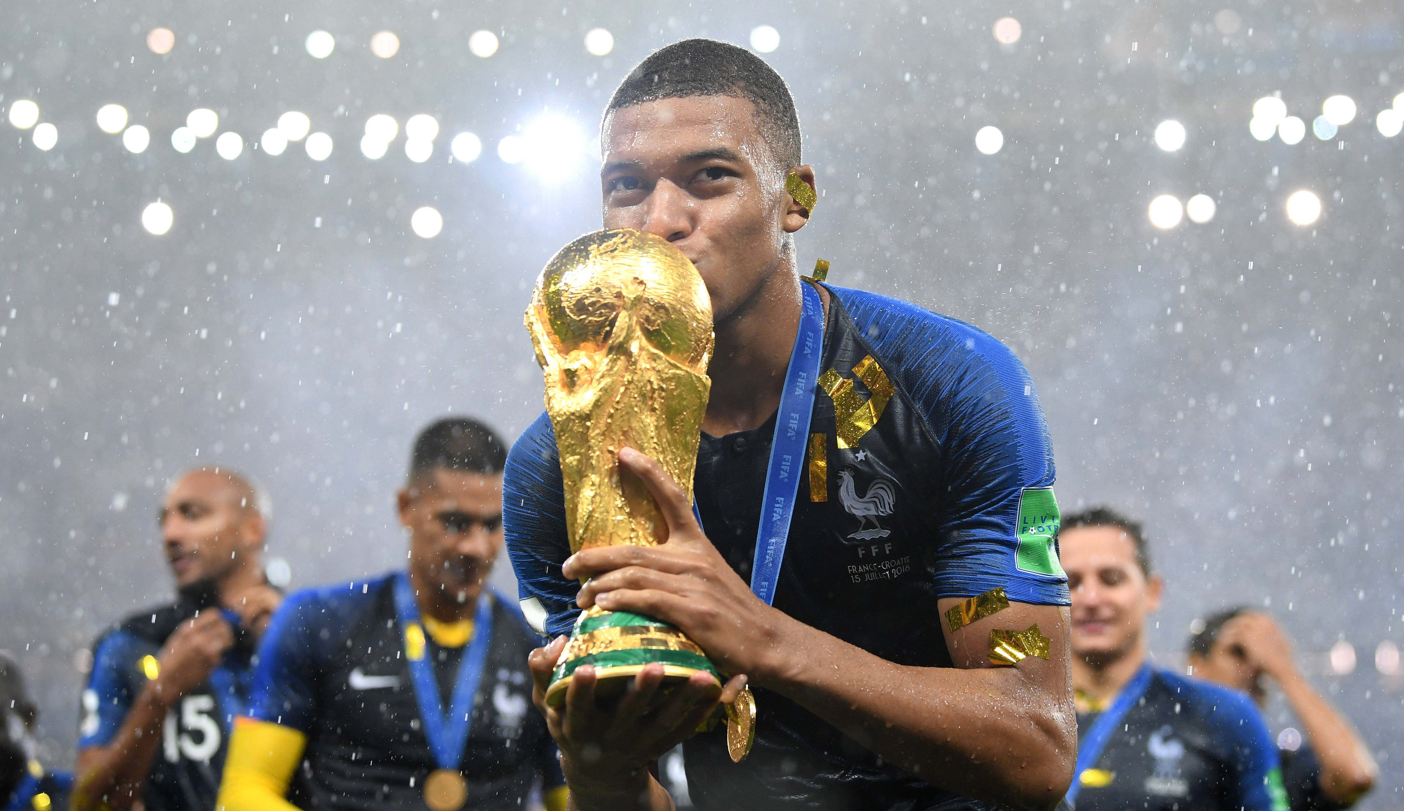 姆巴佩 FIFA 世界盃 壁紙 — 一位勝利的法國足球員在球場燈光下，雨水灑落時親吻閃閃發光的世界盃獎盃。