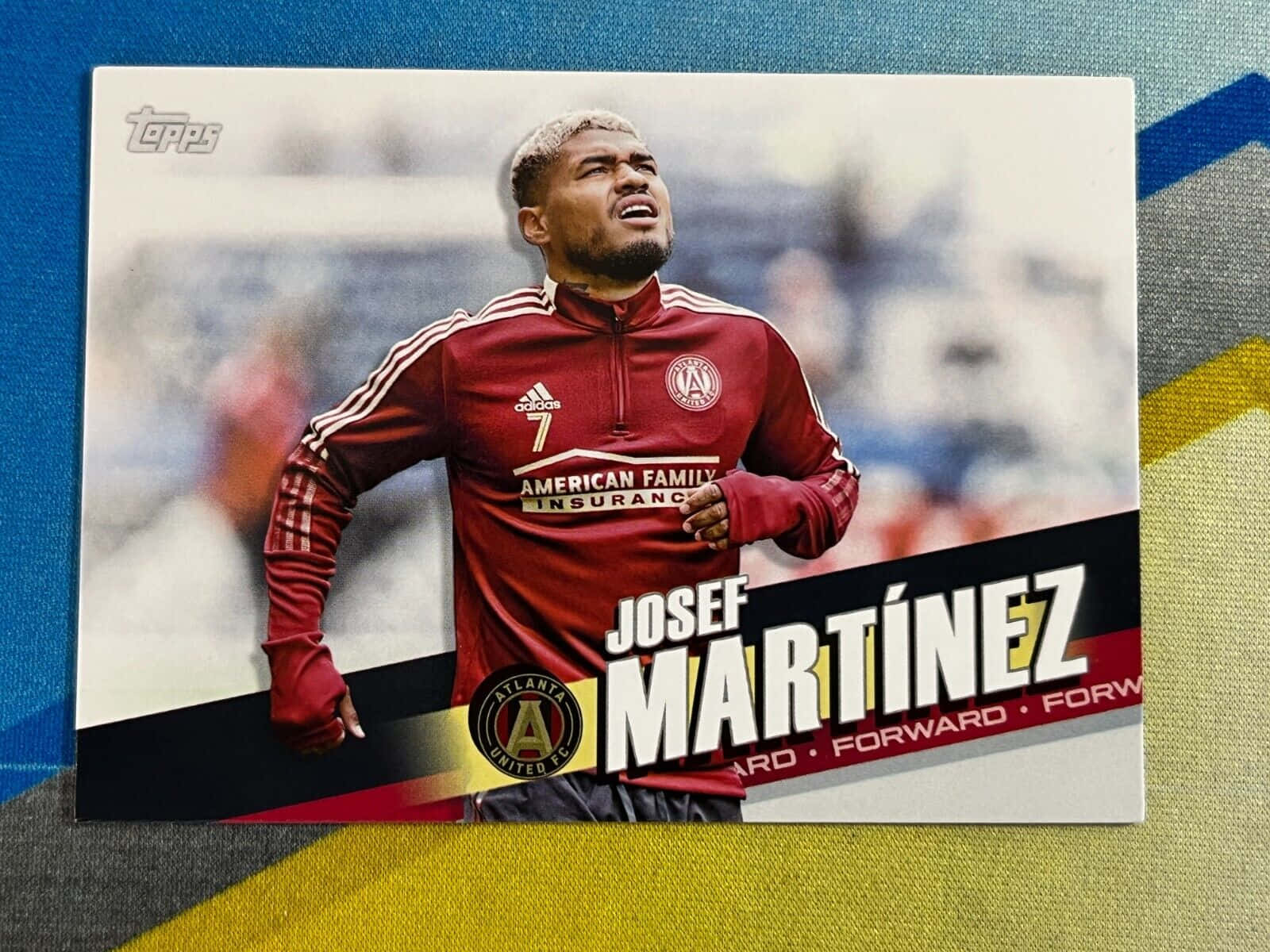 委內瑞拉球員約瑟夫·馬丁內斯 Topps 收藏卡 壁紙 — 一張紅色足球交換卡的特寫，顯示荷西·馬天尼斯正在比賽中，卡片放在色彩繽紛的條紋布料背景上。