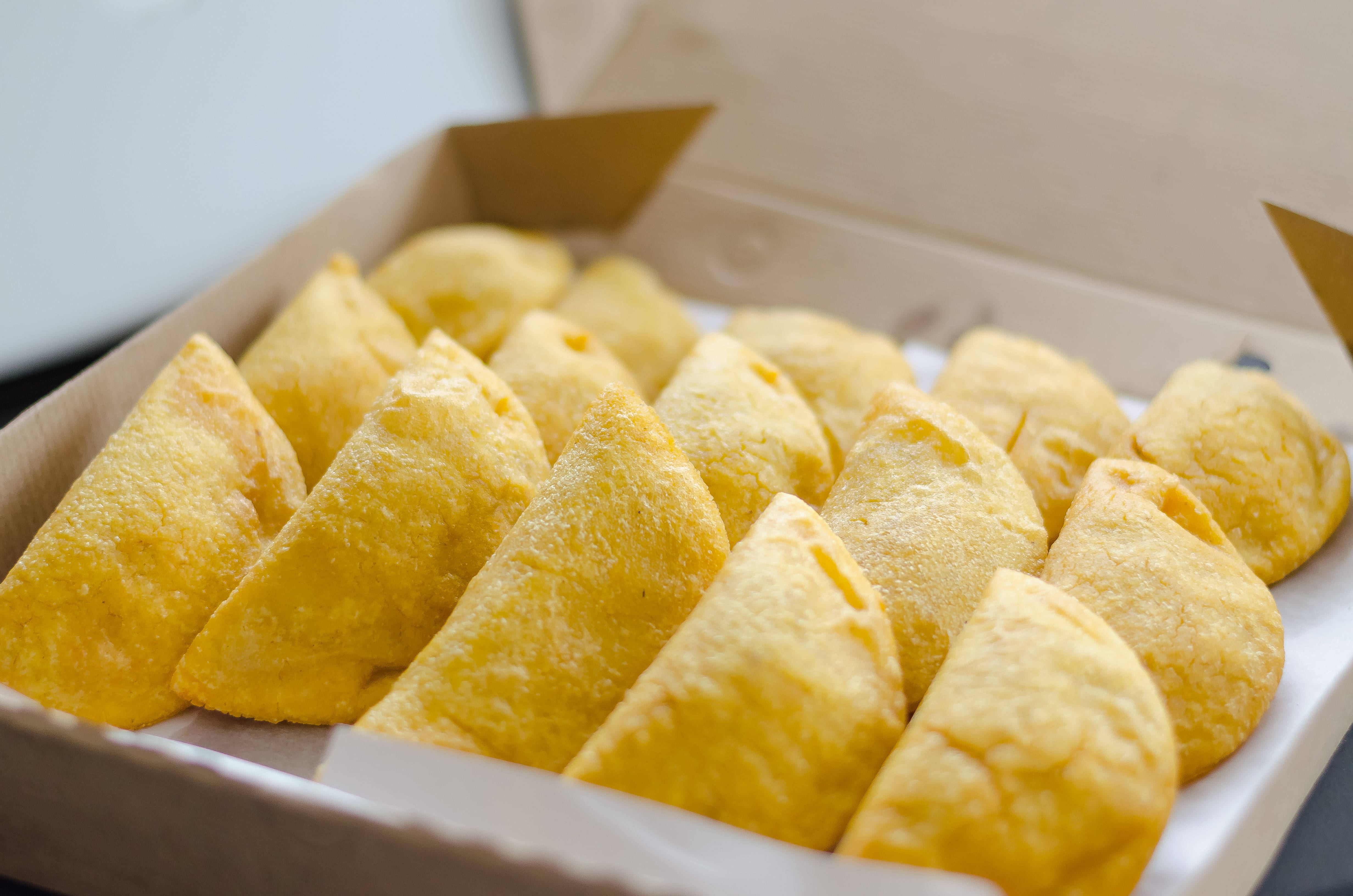 委內瑞拉美味餃子 壁紙 — 金啡色三角形糕點整齊排列在紙箱中，柔和燈光突顯其酥脆質感。