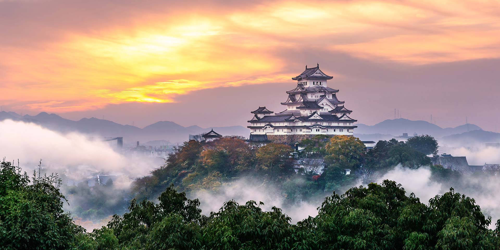 古老的日本城堡在日出時分聳立於霧氣繚繞的山巒之上。