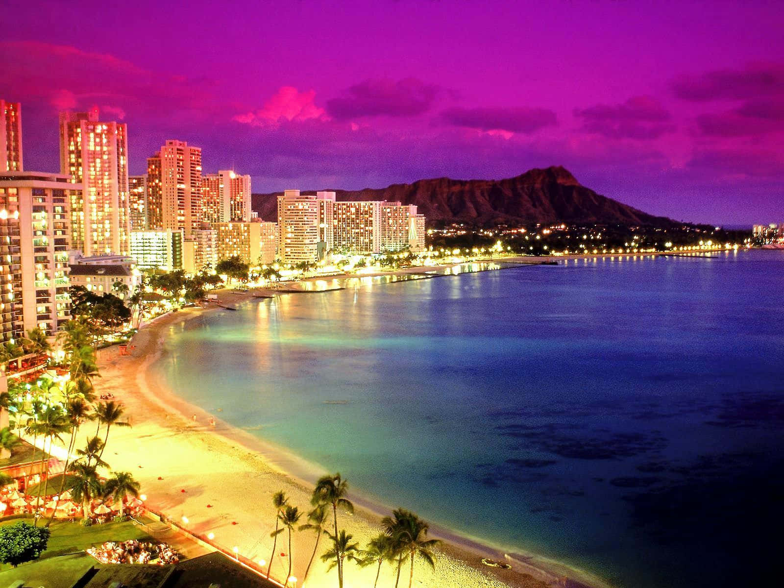Hawaiian Beach 桌布 壁紙 — 威基基海灘上充滿活力的紫色日落，城市燈光在碧綠的海水上閃爍，遠處的鑽石頭山。