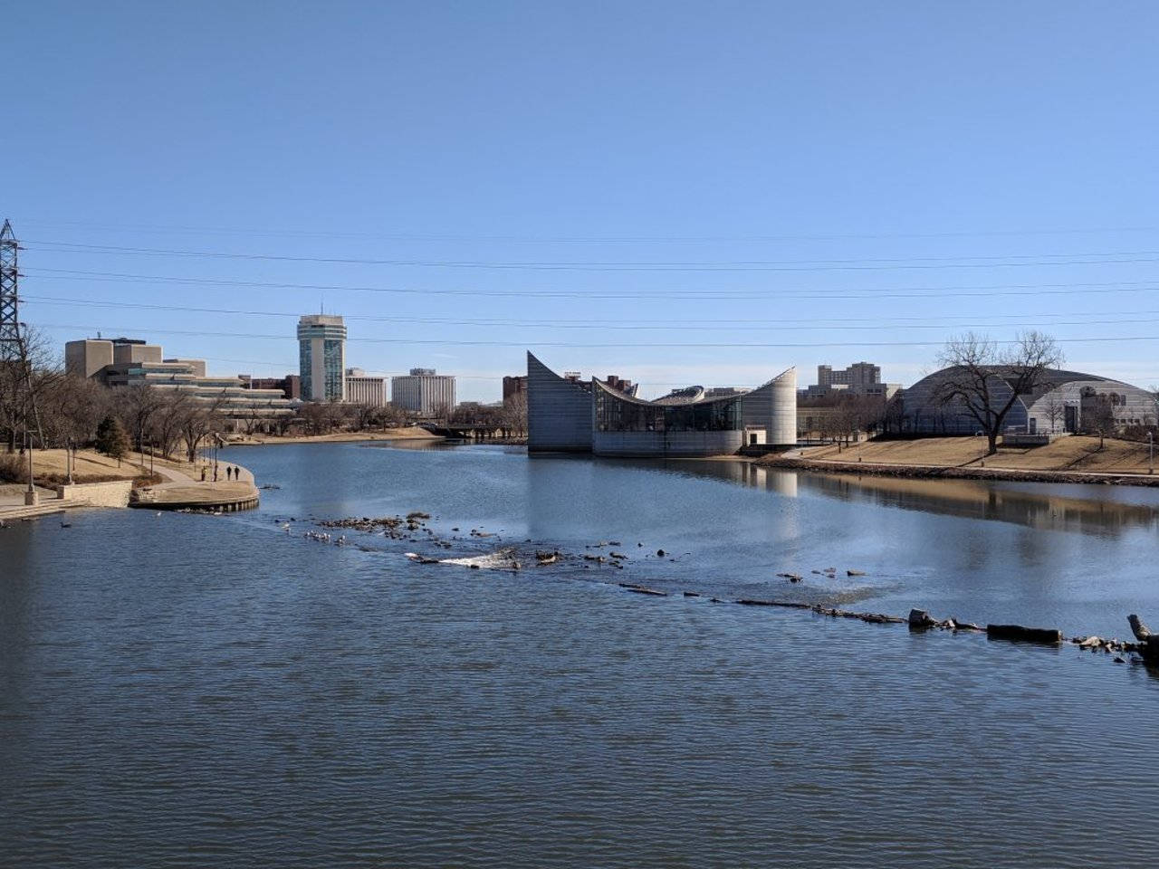 城市河流，有現代建築和光禿樹木，在清澈藍天下