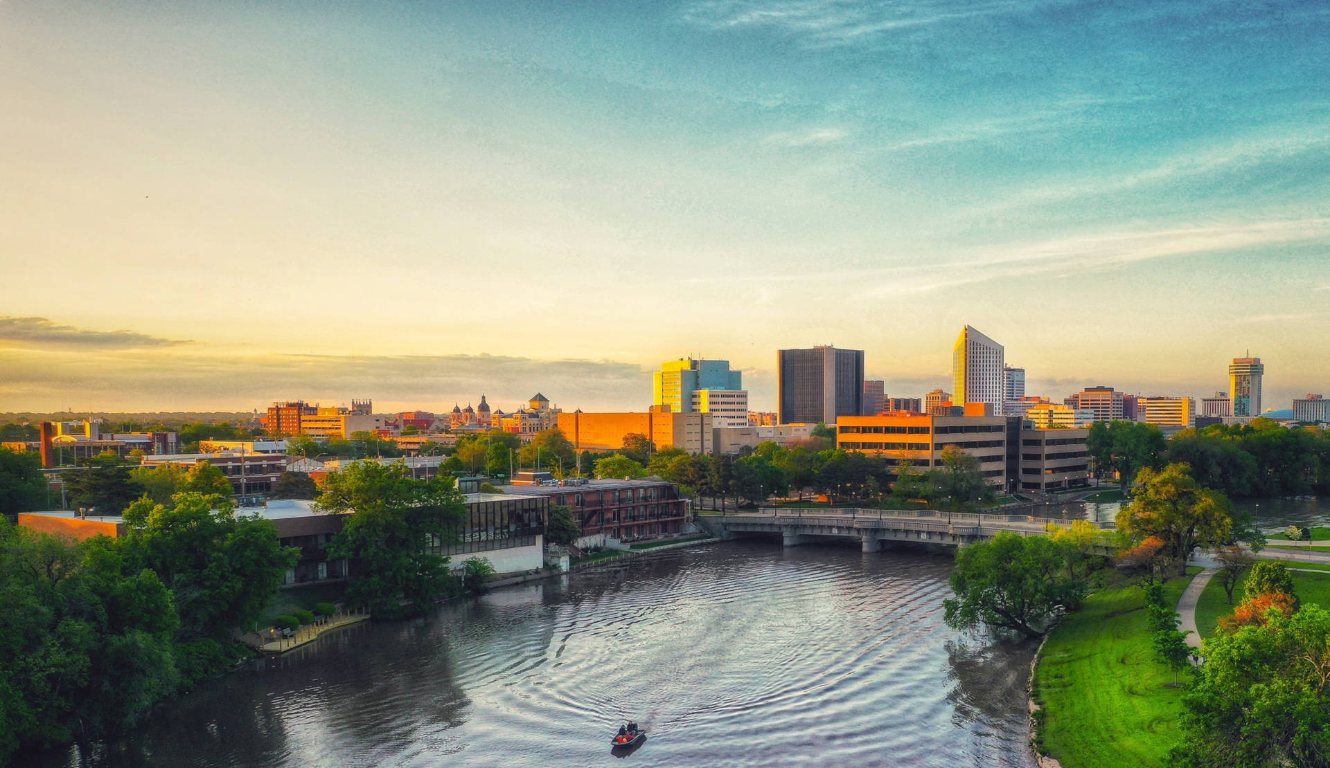 夕陽下的城市天際線，河流和橋樑被綠樹環繞。