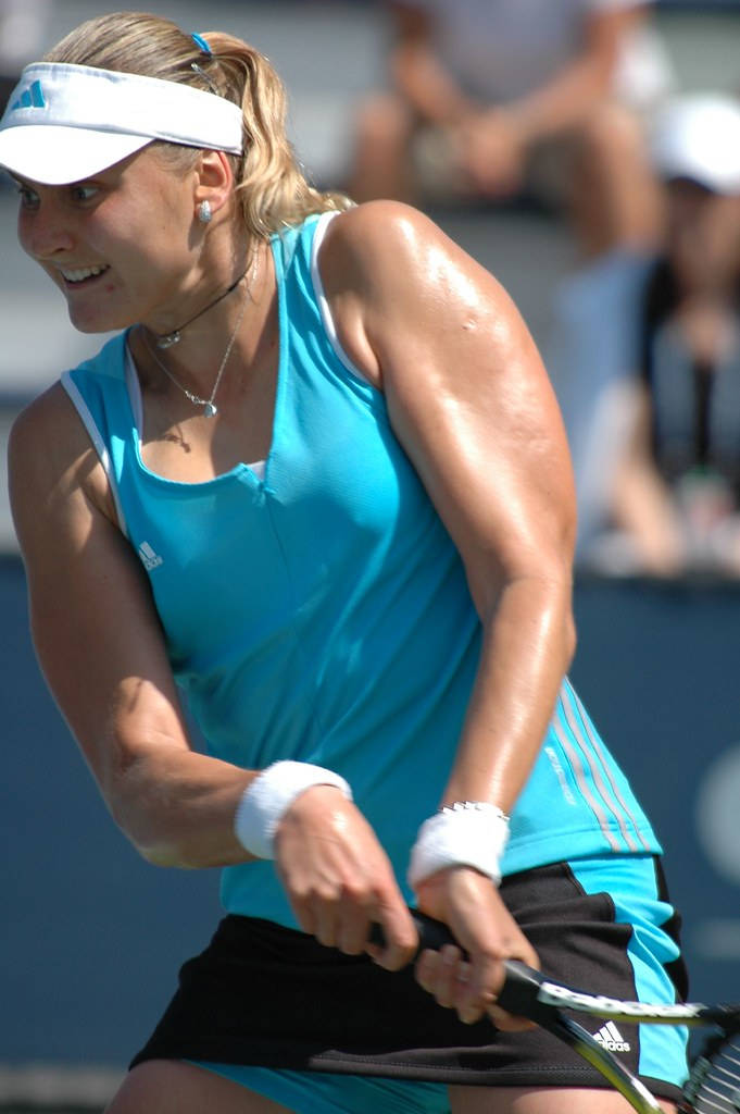 娜迪亞·彼得羅娃球拍下垂姿勢 壁紙 — 一位身穿藍色背心及白色遮陽帽的女網球運動員在強烈陽光下專注地揮拍。