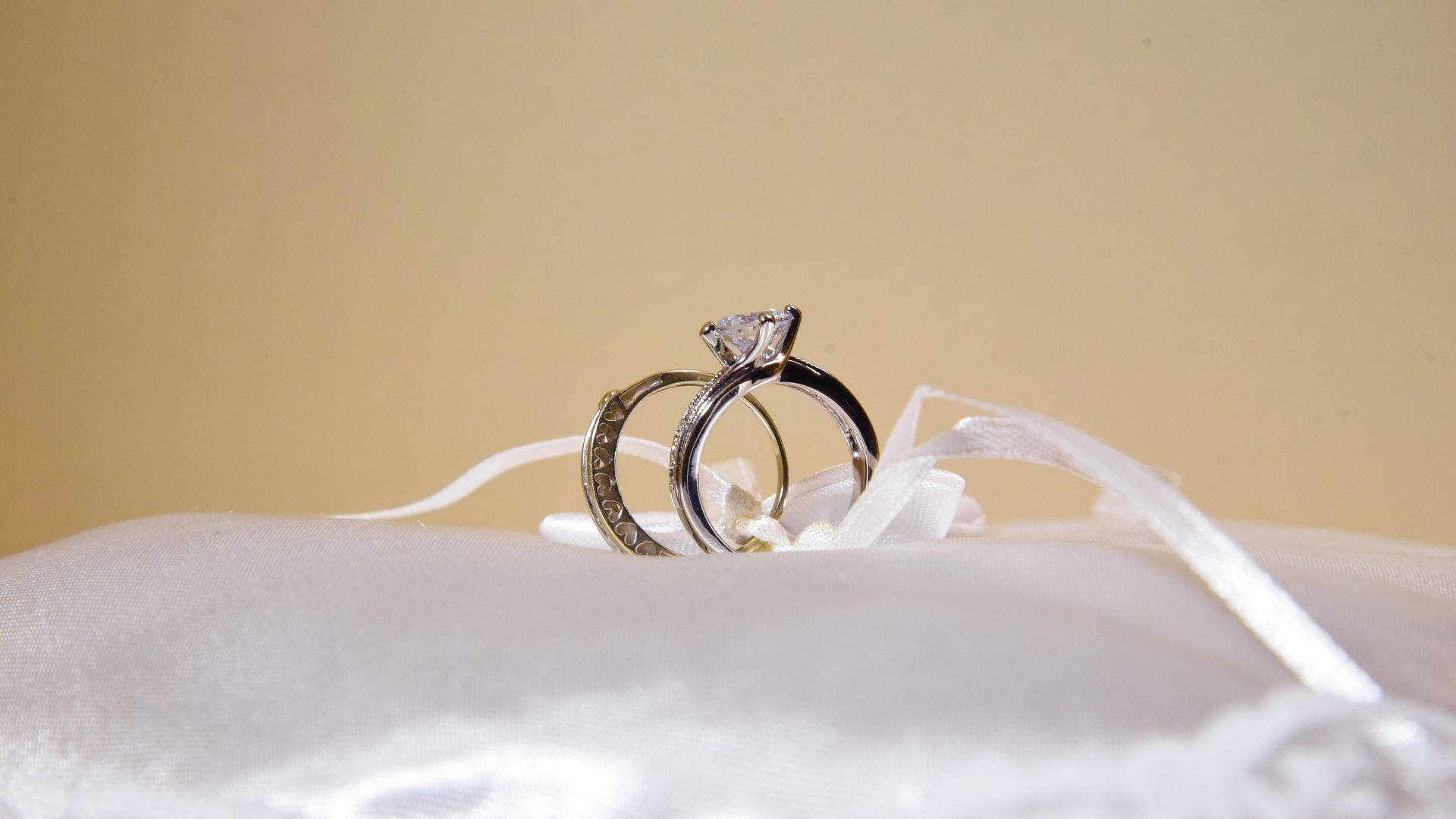 兩枚結婚戒指放在白色緞面枕頭上，背景為米色。