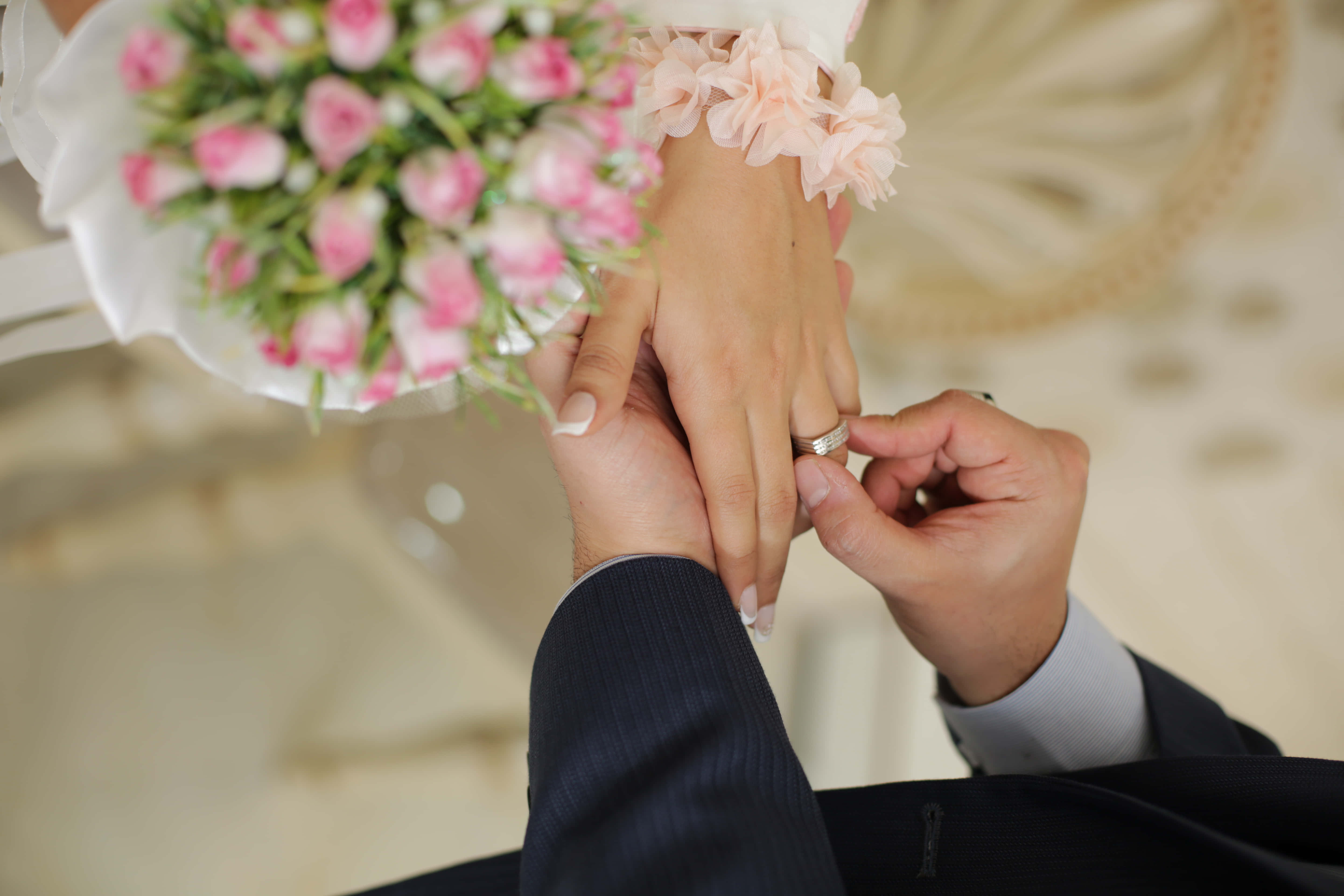 婚紗情侶與粉紅花束 壁紙 — 新郎輕輕地將結婚戒指戴在新娘的手指上，而她正拿著一束粉紅玫瑰。