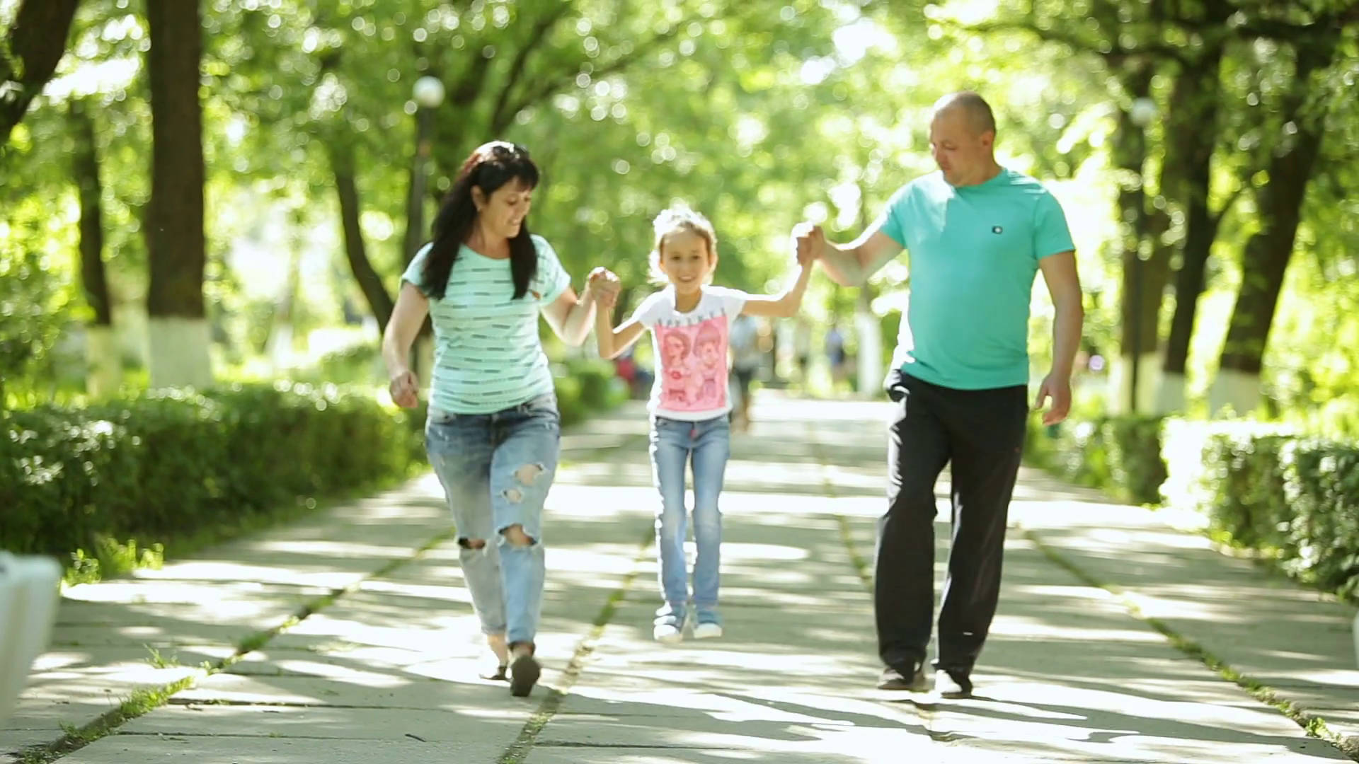 媽媽與爸爸公園 壁紙 — 一個幸福的三口之家在陽光明媚的夏日，手牽手走在綠樹成蔭的公園小徑上。
