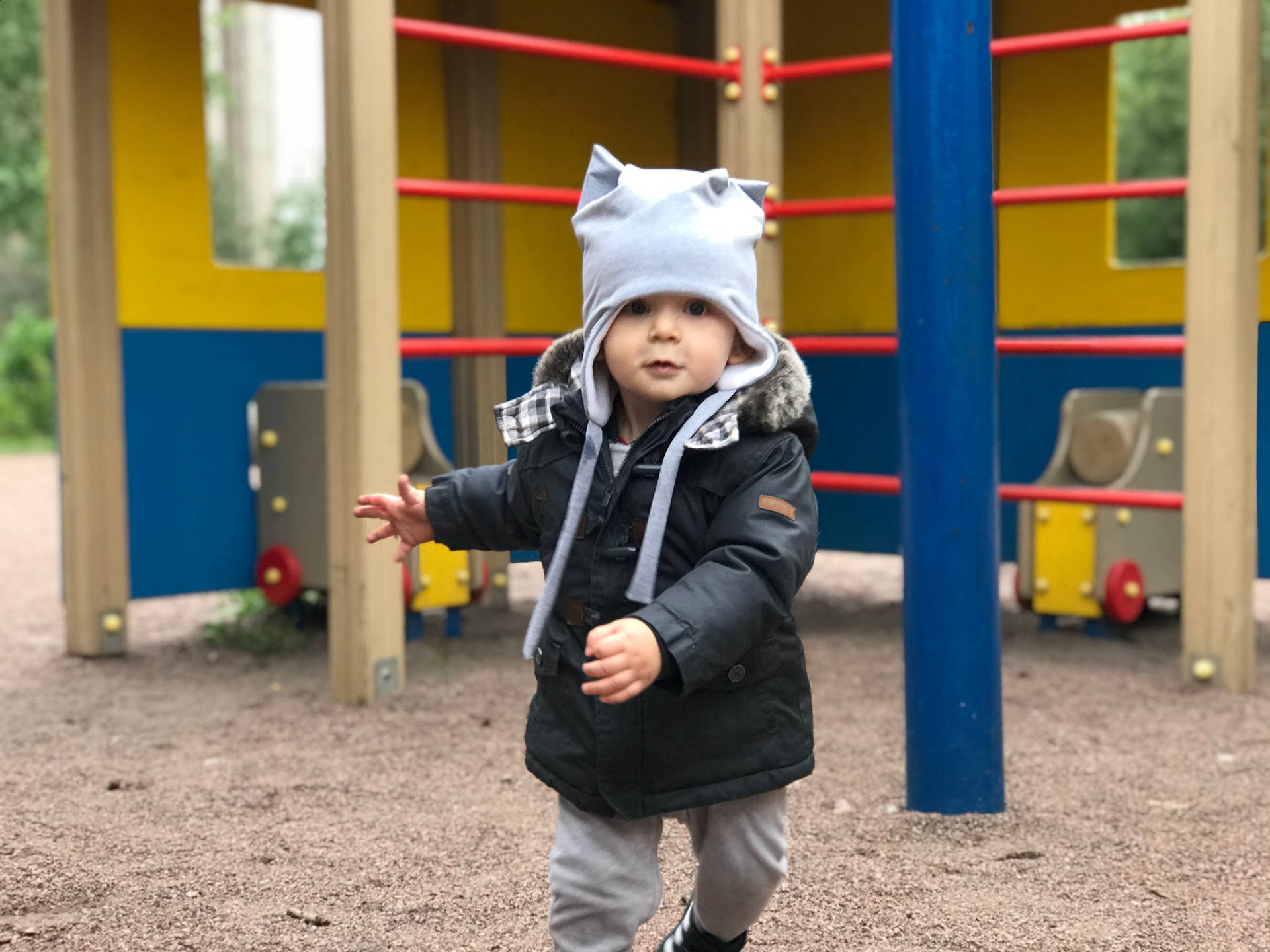 一個戴著貓耳帽和冬季外套的幼兒在遊樂場上。