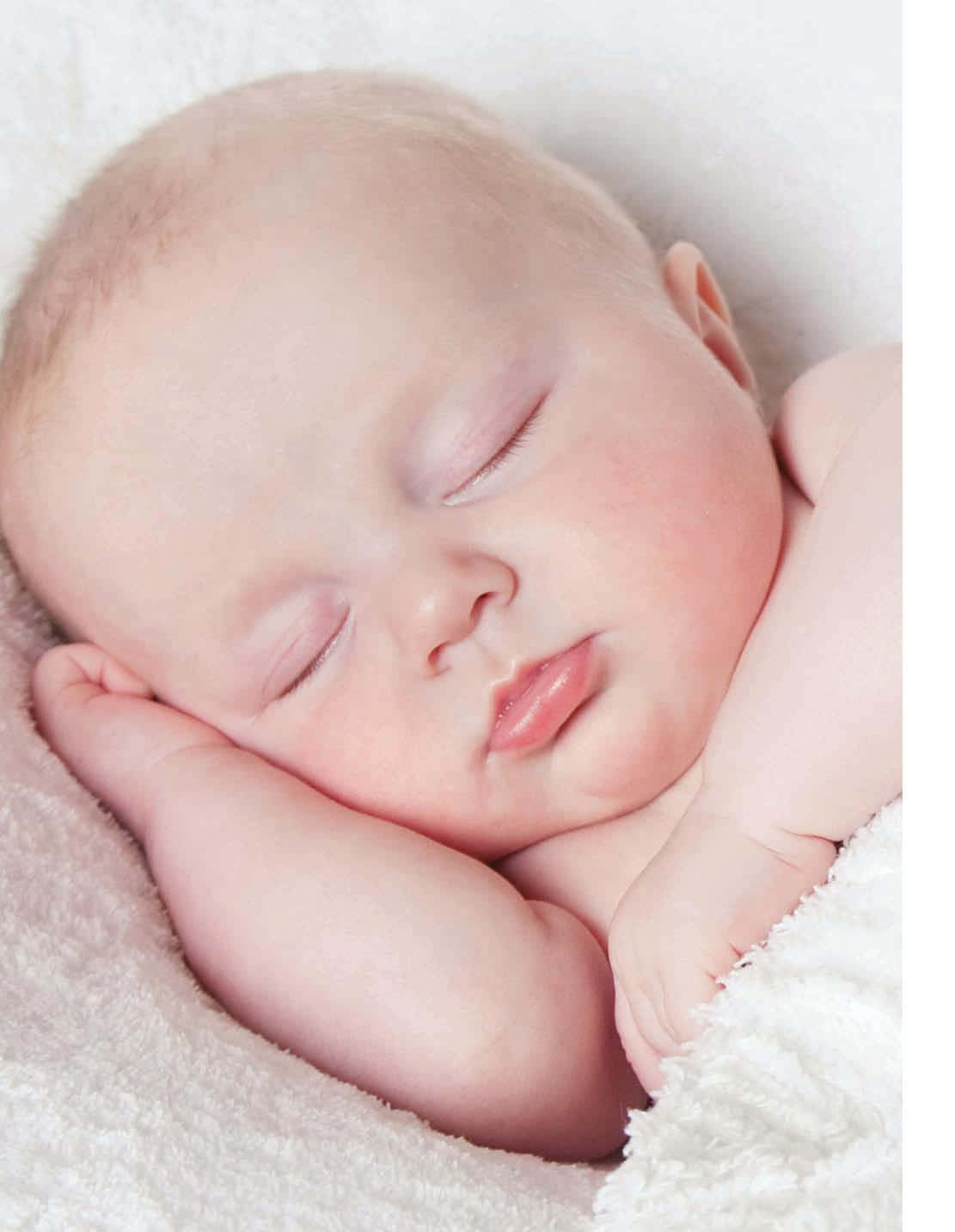 一個睡著的新生嬰兒，雙手放在下巴下，躺在蓬鬆的白色毯子上。