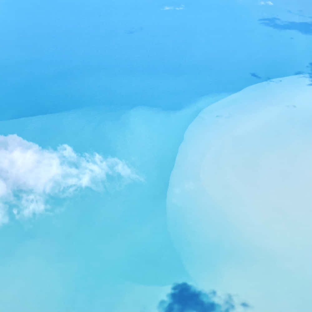 碧綠的海洋與白色沙灘相接，下方飄浮的雲朵從上方觀看。