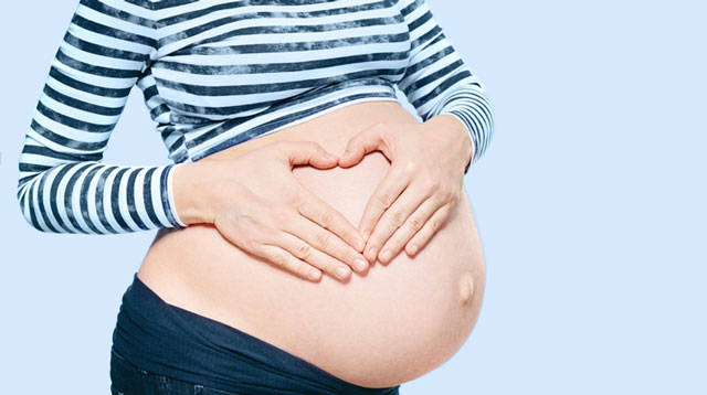 孕婦用雙手在肚子上方做出心形。
