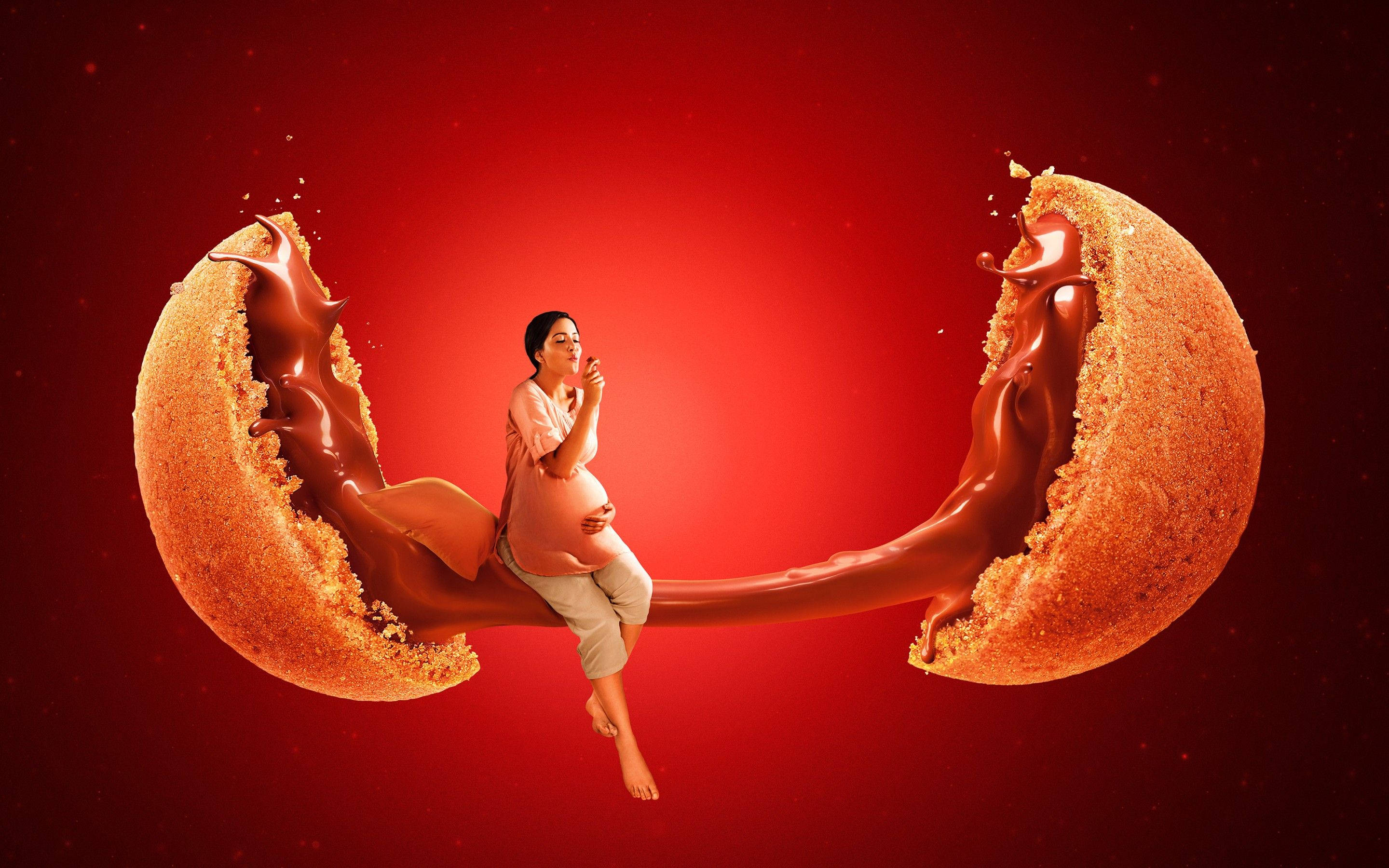 孕婦與黑奇幻巧克力 壁紙 — 一名孕婦優雅地坐在一個裂開的巨型朱古力曲奇上，流動的朱古力襯托著深紅色背景。