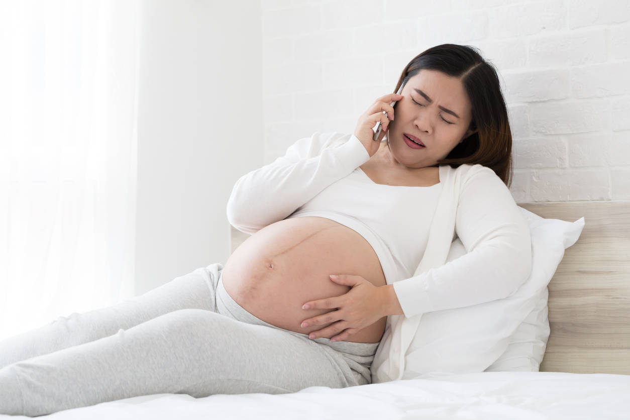 孕婦躺在床上抱著肚子講電話