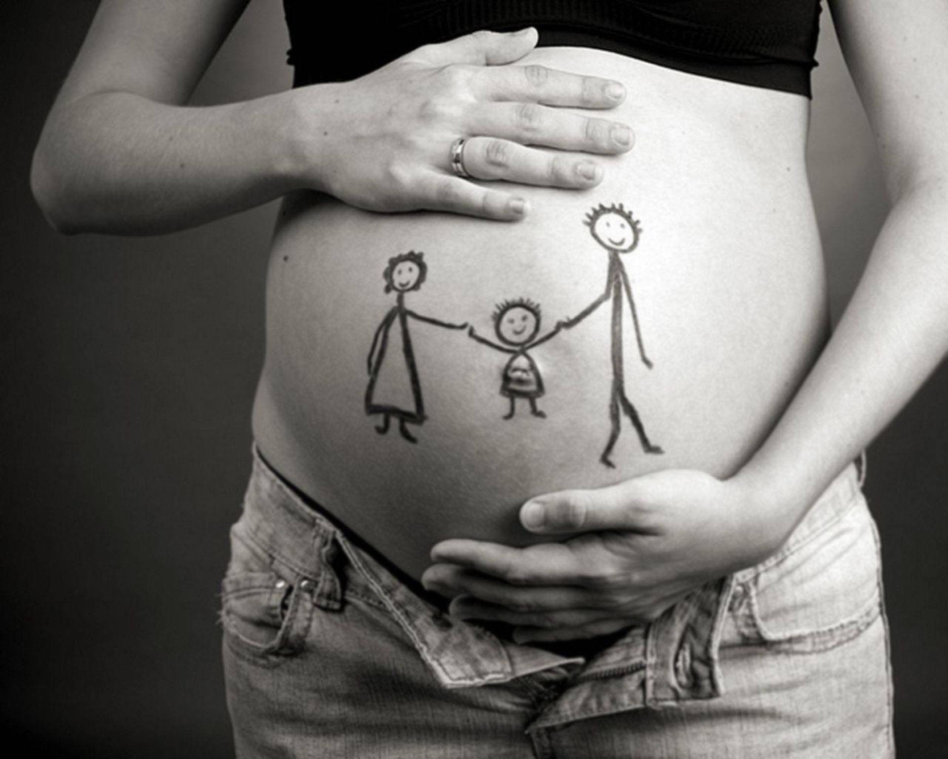 孕肚家庭畫像 壁紙 — 一位孕婦的肚子上有一個孩子氣的畫，畫著三個火柴人牽手，她的雙手輕輕地捧著腹部。