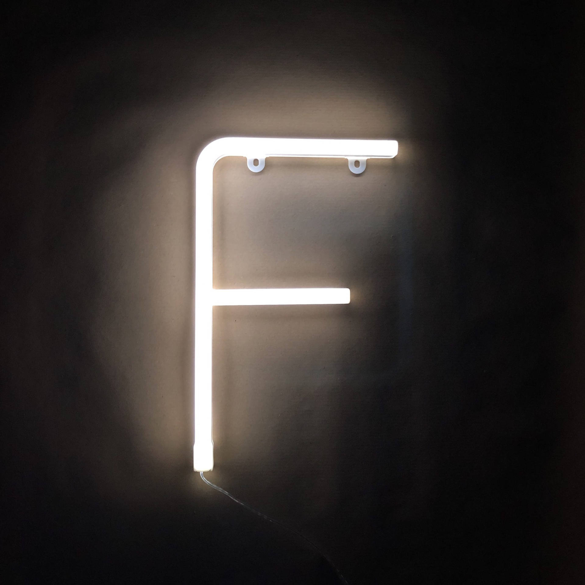 一個明亮的白色霓虹字母F安裝在深色牆壁上。