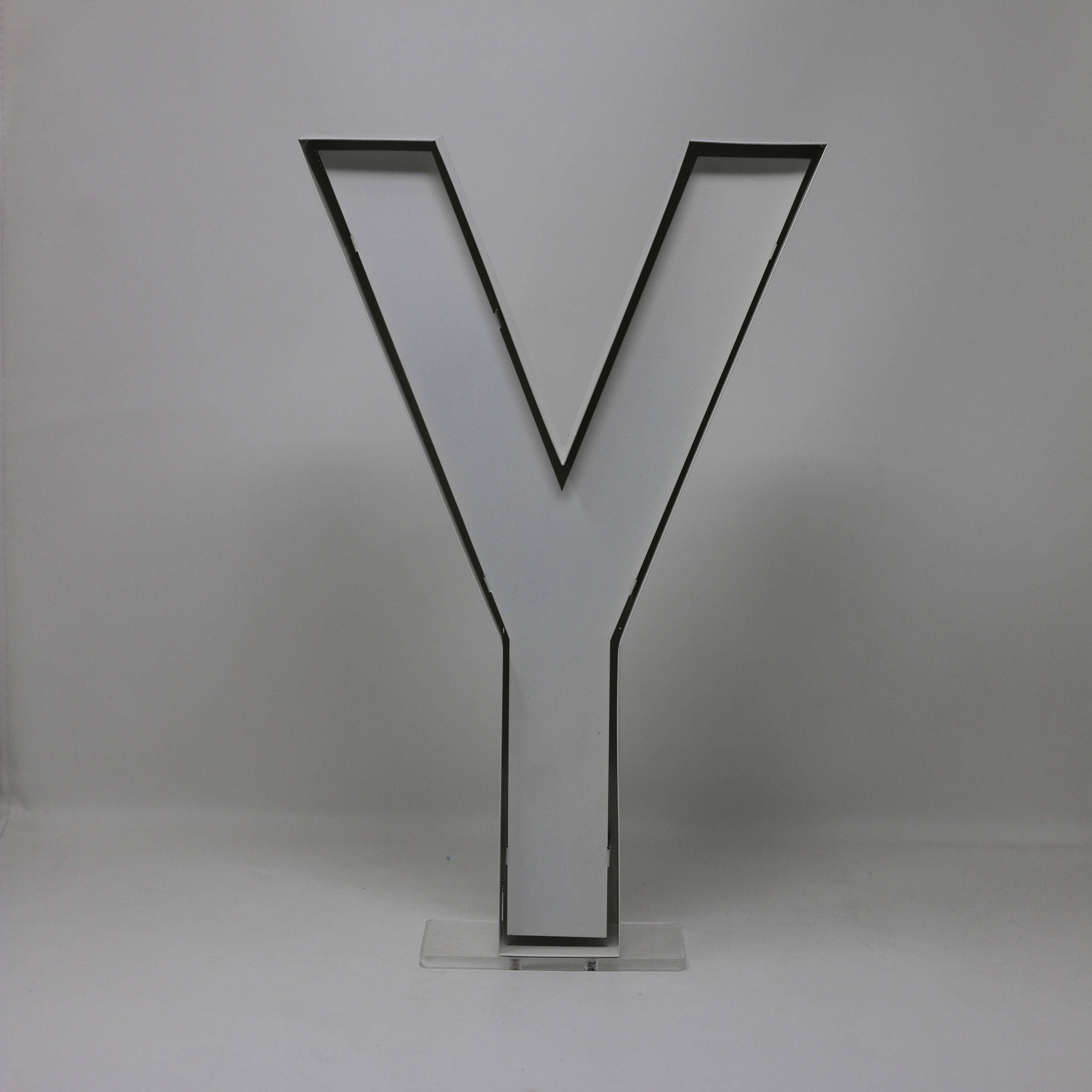 字母Y形LED燈 壁紙 — 一個極簡風格的黑色輪廓字母Y豎立在透明亞加力底座上，背景為純白色。