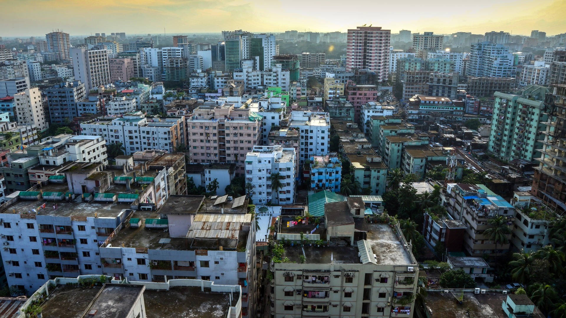 孟加拉國都市化地區 壁紙 — 溫暖天空下，黃金時段密集城市擴張中混合高層和低層建築的鳥瞰圖。