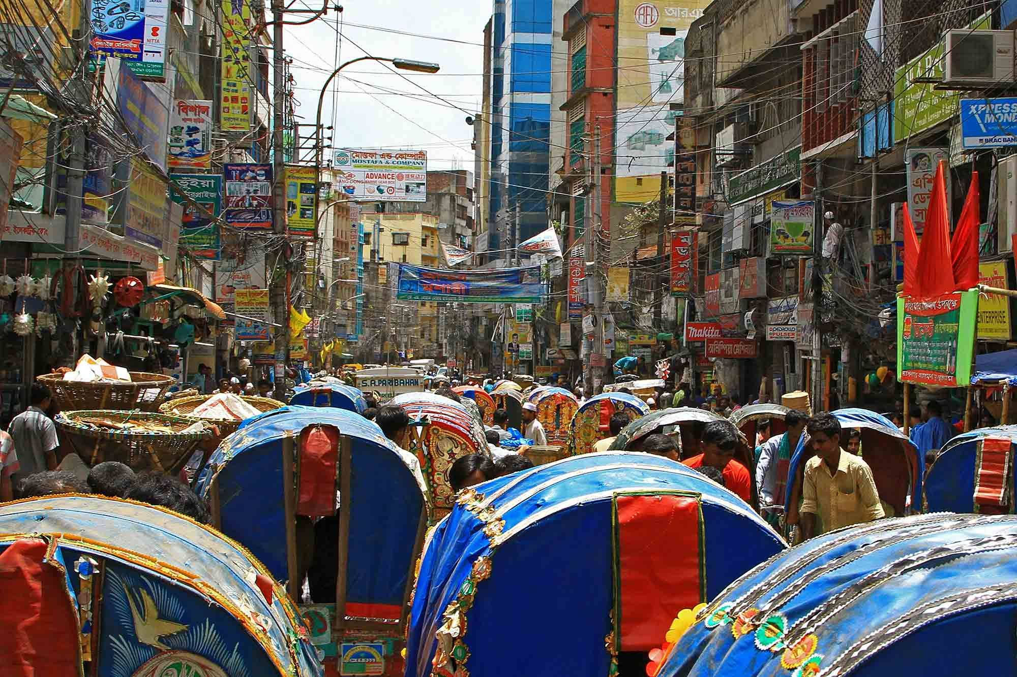 孟加拉達卡繁忙街景 壁紙 — 繁華的都市街道，色彩繽紛的人力車和擁擠的商店，天空明亮。