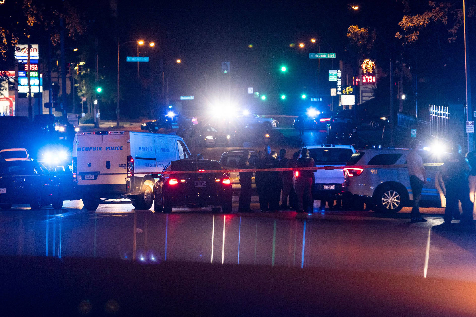孟菲斯市中心日落風景 壁紙 — 夜間城市街道場景，警車閃爍燈光，警員站在犯罪現場的封鎖線後。