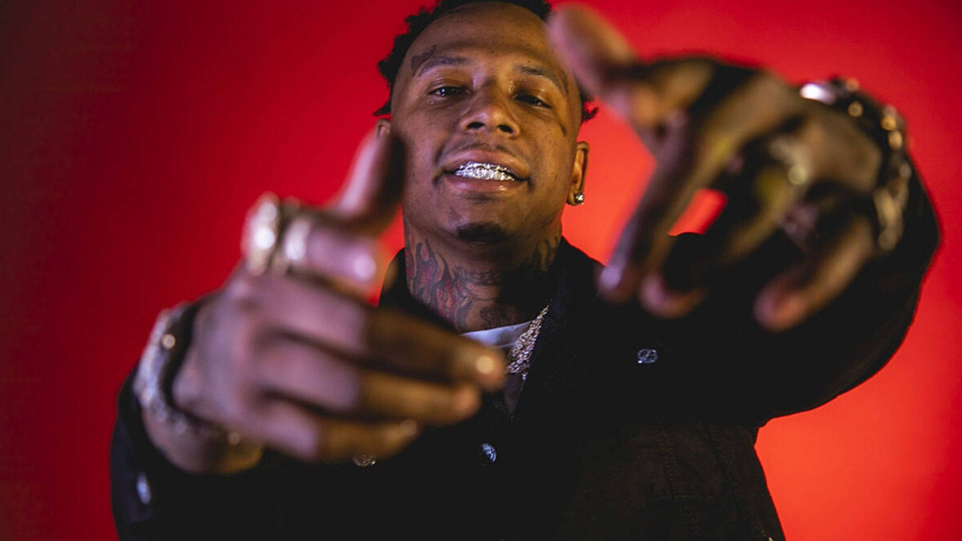 孟菲斯饒舌歌手 Moneybagg Yo 壁紙 — 一名有紋身和鑽石牙套的男子在鮮紅色背景前微笑，手指向前方。