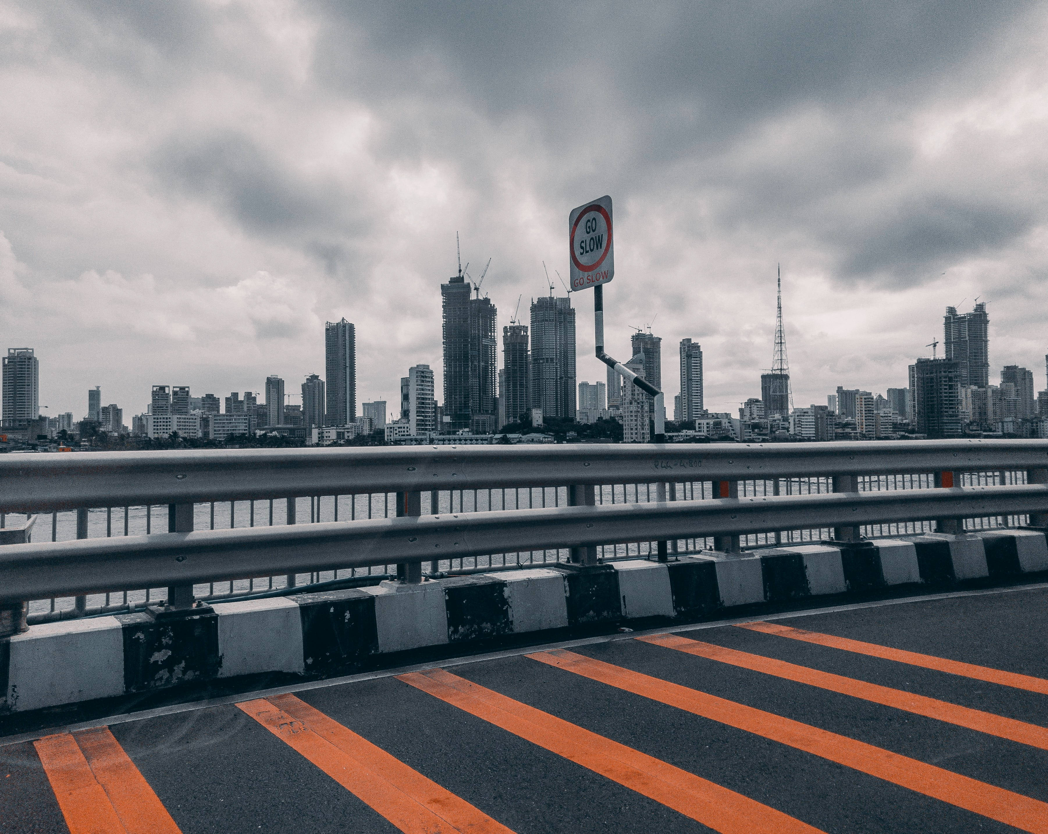 孟買班德拉-沃利海峽大橋 壁紙 — 一條充滿陰鬱氣氛的城市橋樑，帶有醒目的橙色條紋，通往雲霧繚繞的城市天際線，高聳的摩天大樓正在建設中。