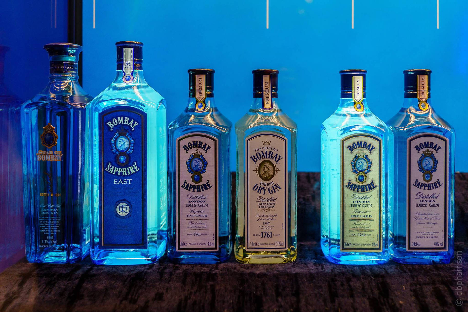 六個 Bombay Sapphire 氈酒瓶在藍色燈光下排列在木質吧檯上。