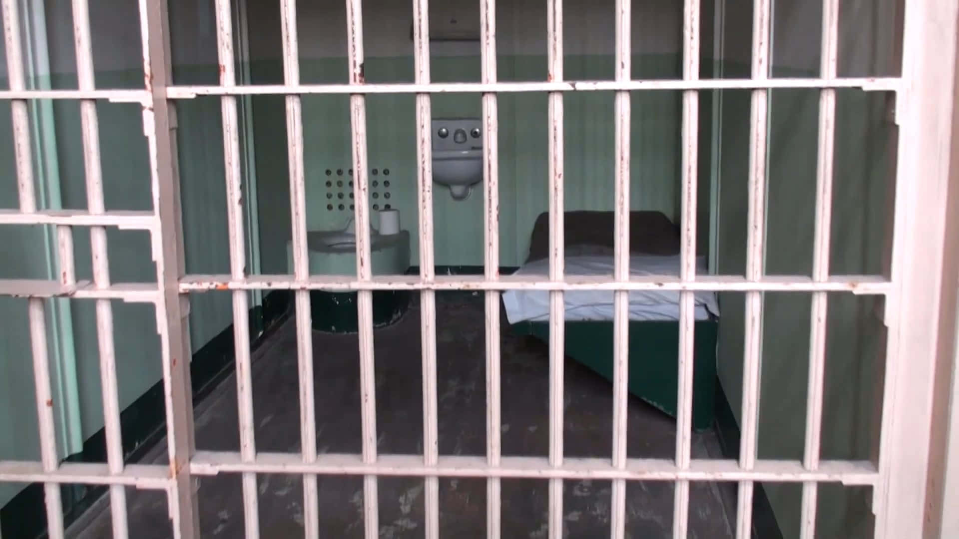 生鏽的監獄欄杆框住了一個只有床和水槽的空蕩牢房。