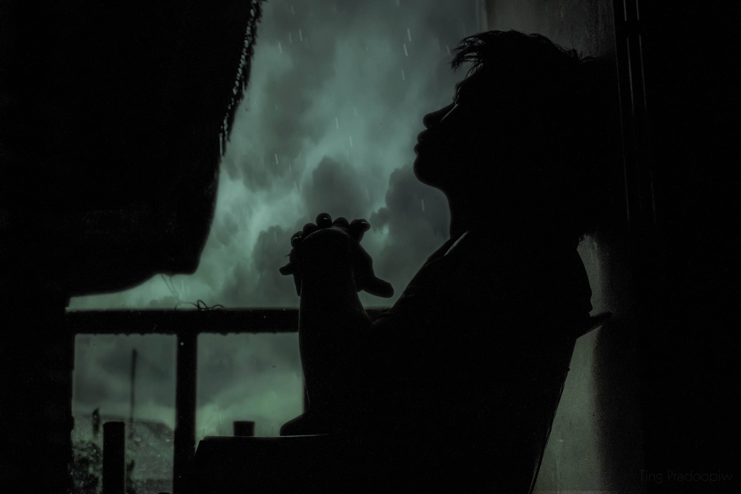 孤寂雨夜中的傷心男孩 壁紙 — 一個人在暴風雨中對著帶有綠色的窗戶祈禱的剪影，窗外下著雨。