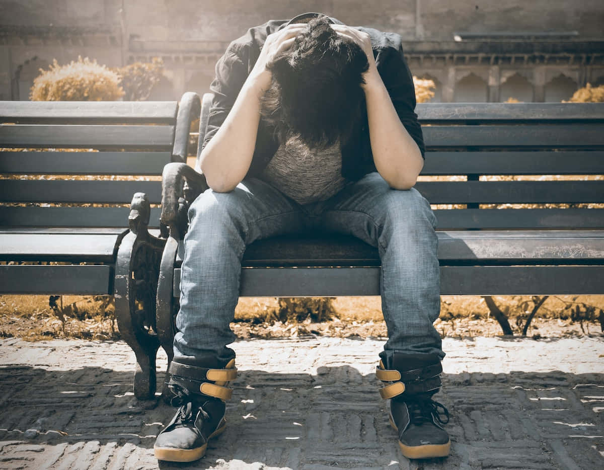 坐在長椅上雙手抱頭看起來很痛苦的人