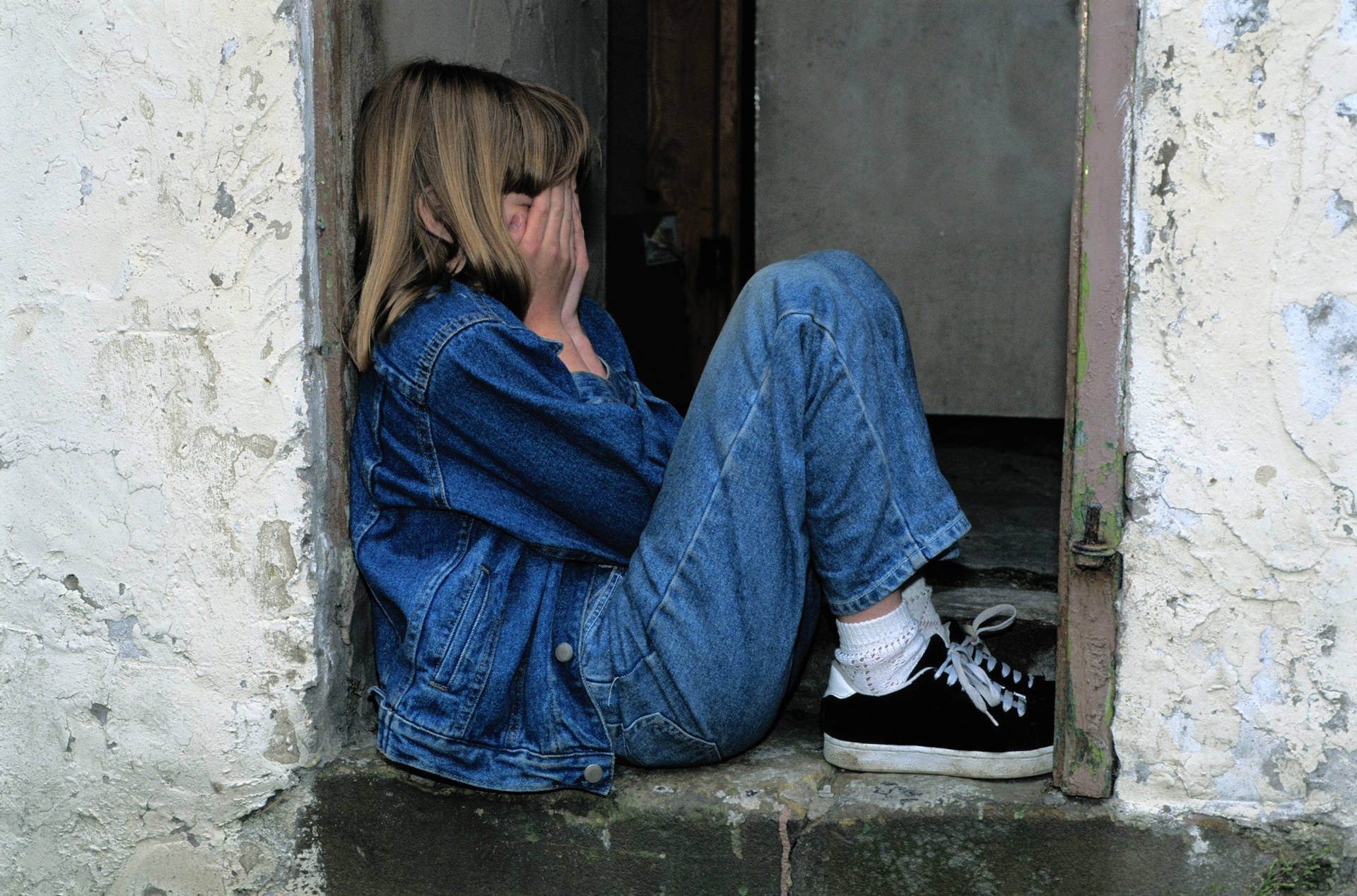 一個穿著牛仔布的女孩坐在門口時遮住臉。