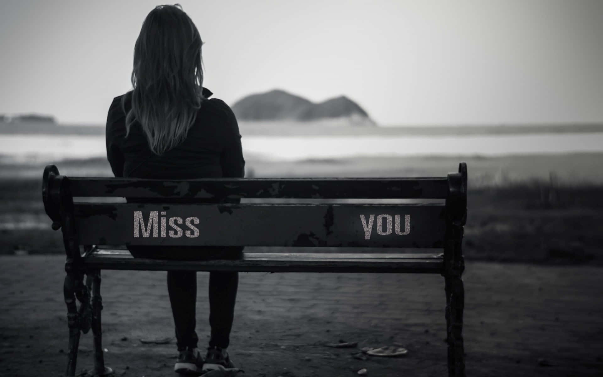 水邊長椅上坐著一個人，椅背上有「Miss you」字樣