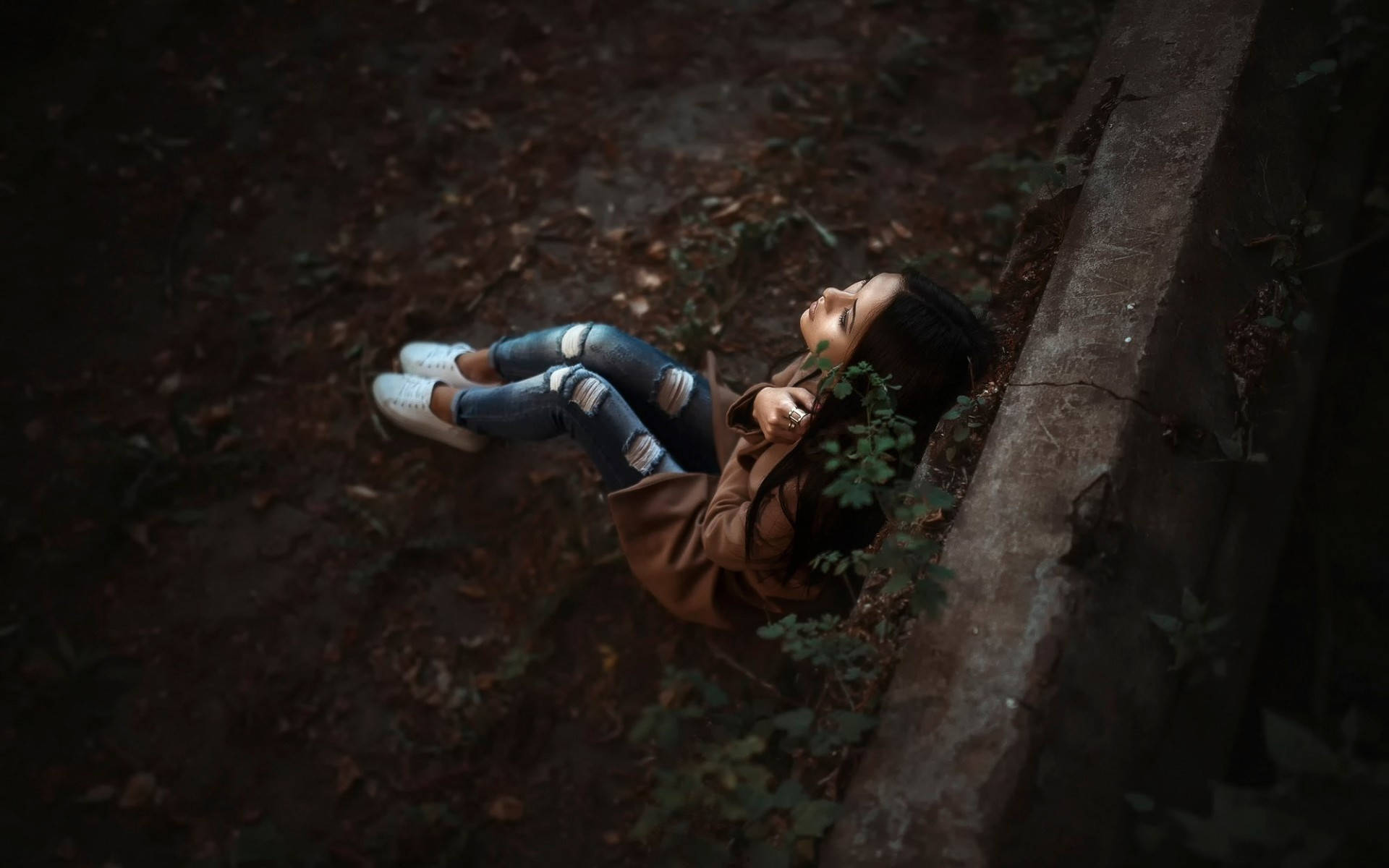 孤獨女孩 壁紙 — 一位年輕女性躺在森林地面上，旁邊有一塊長滿青苔的石頭，她抬頭仰望，表情平靜，周圍散落著秋天的落葉。