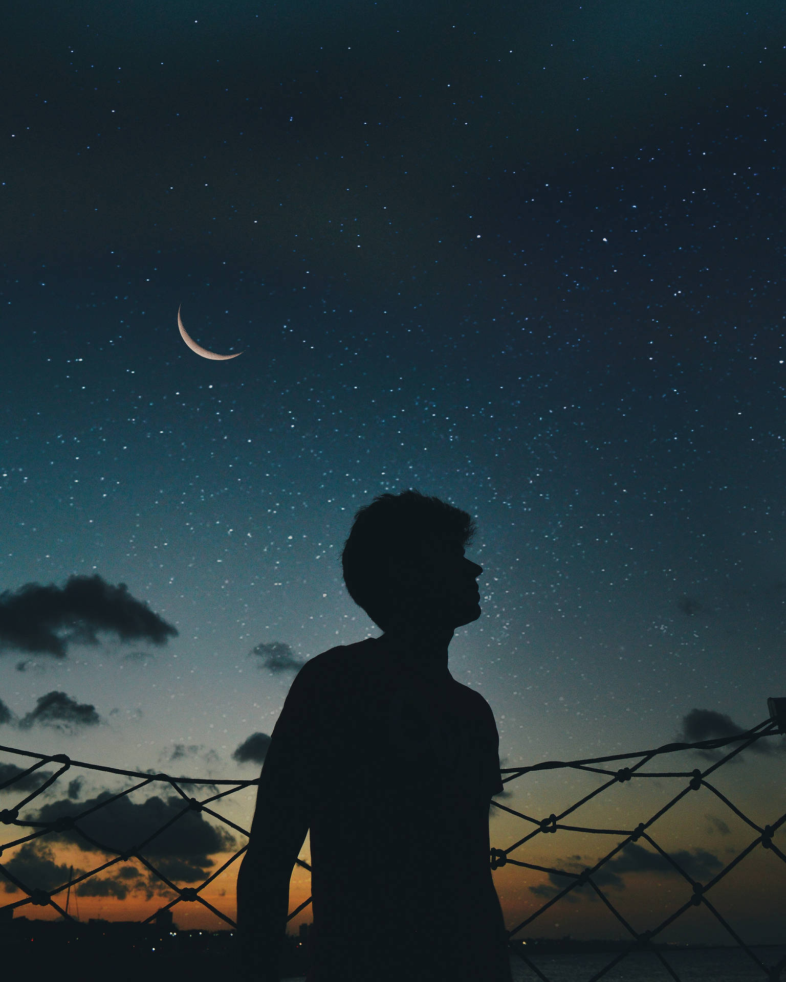 夜晚透過圍欄觀看彎月和星星的人的剪影。