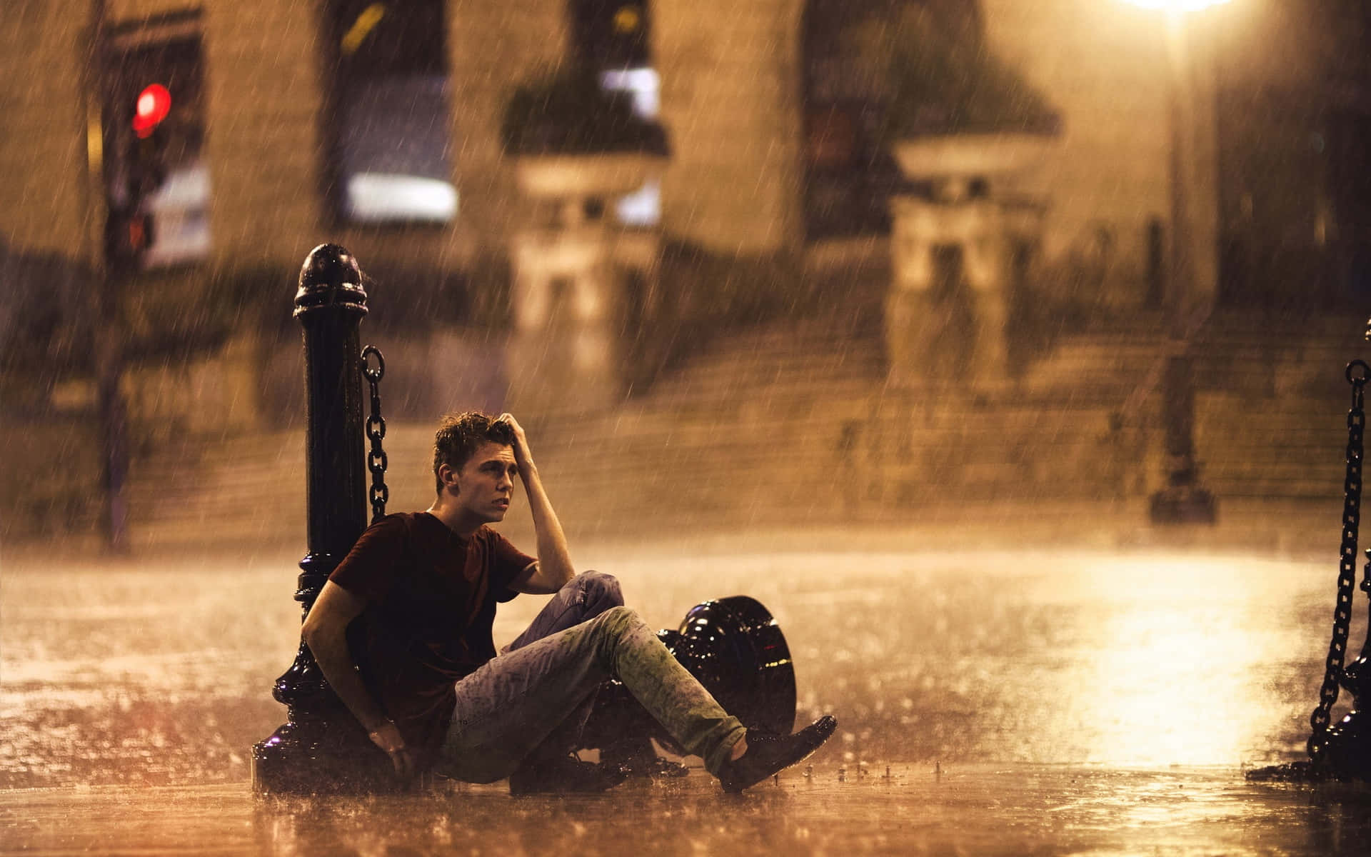 孤獨男子沉思 壁紙 — 一名年輕男子在暴雨期間獨自坐在城市環境中路燈下的洪水中。