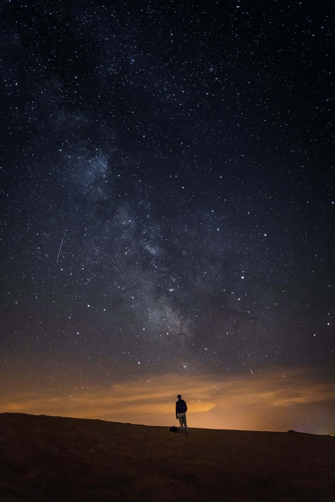 一個人獨自站在沙漠沙丘上，在星空下，銀河清晰可見。