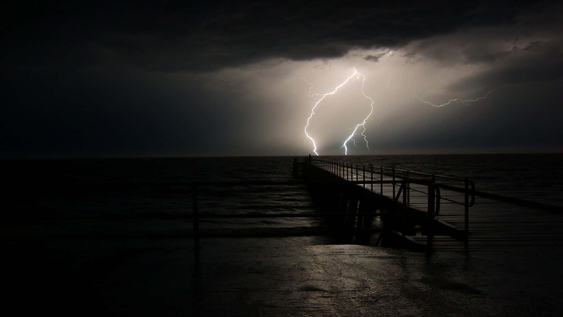 Thunderstorm 桌布 壁紙 — 孤獨的碼頭延伸至波濤洶湧的大海，一道耀眼的閃電劃破黑暗的天空。