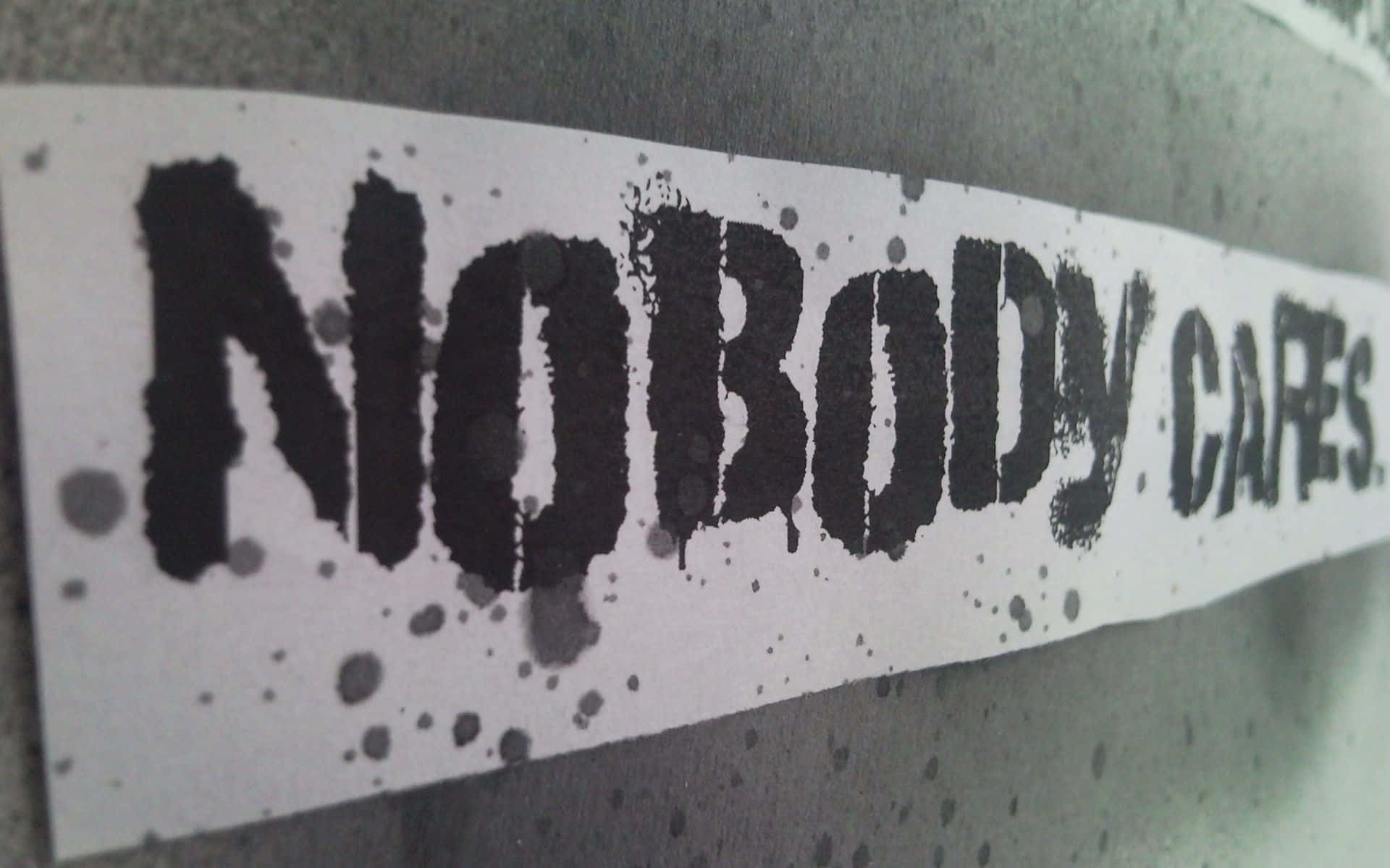 一張黑色模板貼紙，上面寫著「NOBODY CARES」，貼在帶有墨水飛濺的灰色牆上。