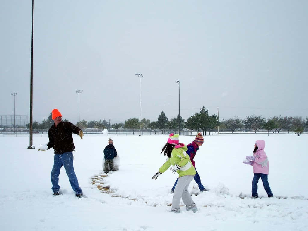 Snowball Fight 桌布 壁紙 — 孩子們和一位成人在多雲的天空下，於廣闊的雪地上開心地擲雪球。