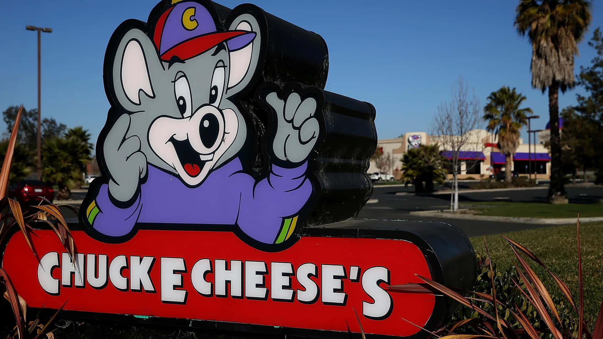 Chuck E Cheese 吉祥物雕像在陽光普照的日子於餐廳入口揮手。
