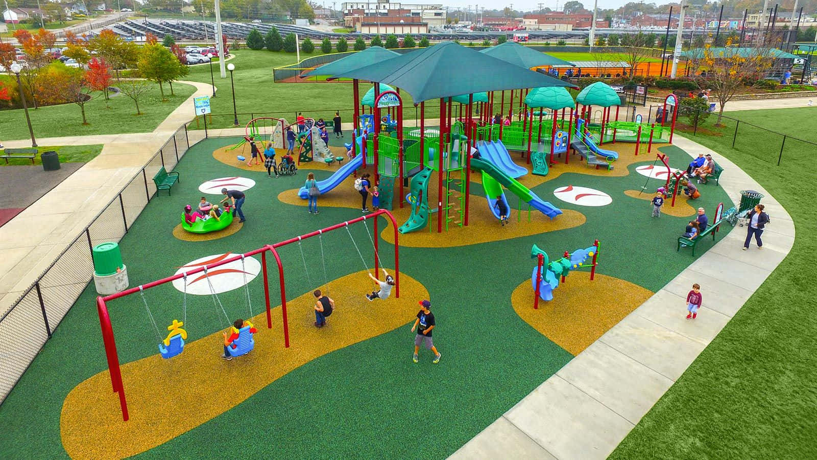 Playground 桌布 壁紙 — 孩子們在色彩繽紛的滑梯和鞦韆上玩耍，周圍是秋日樹木環繞的充滿活力的戶外遊樂場。